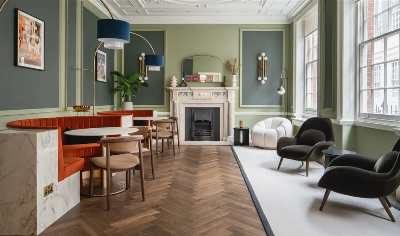 Interior of a stylish living room with green walls, large windows, modern furniture, and a fireplace.