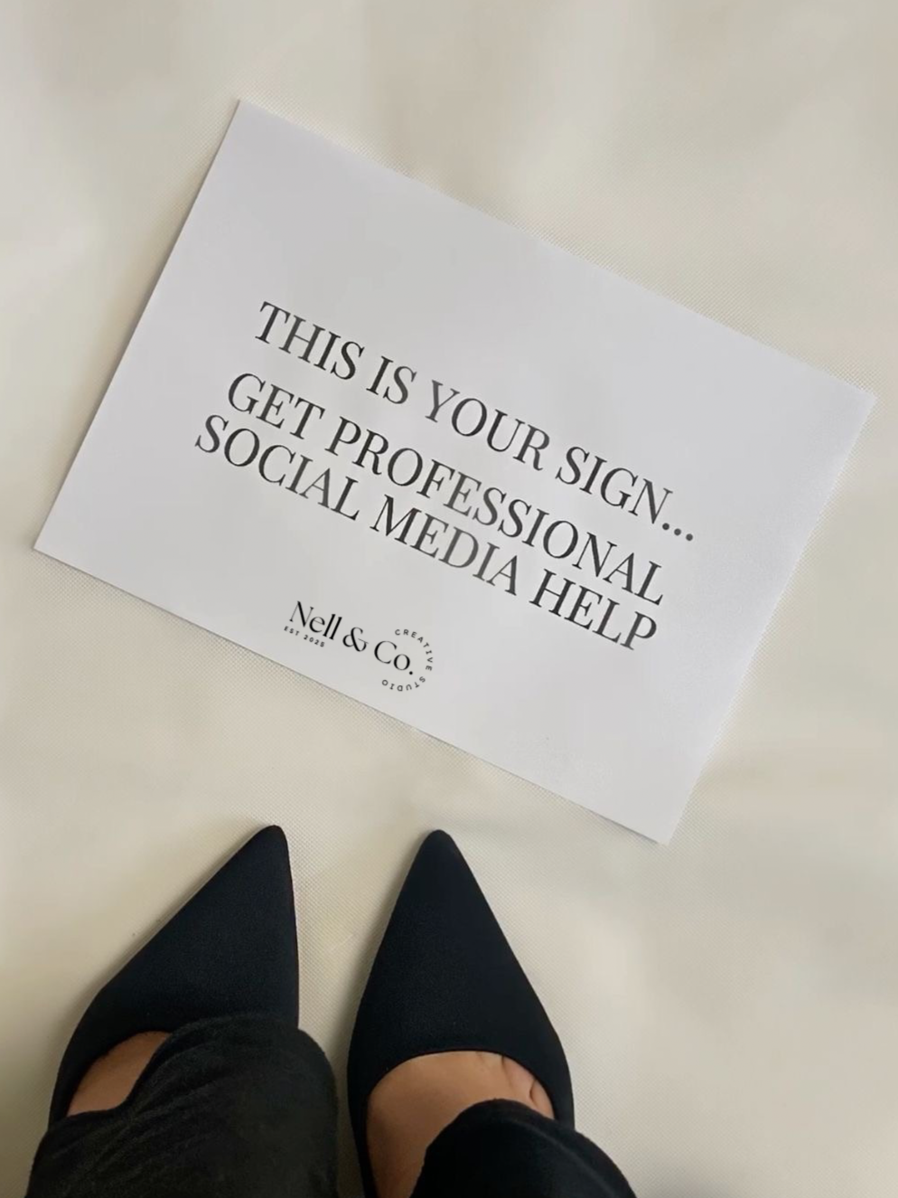 Sign on the floor that reads: "This is your sign... Get professional social media help" with a person wearing black high heels and black pants standing nearby.