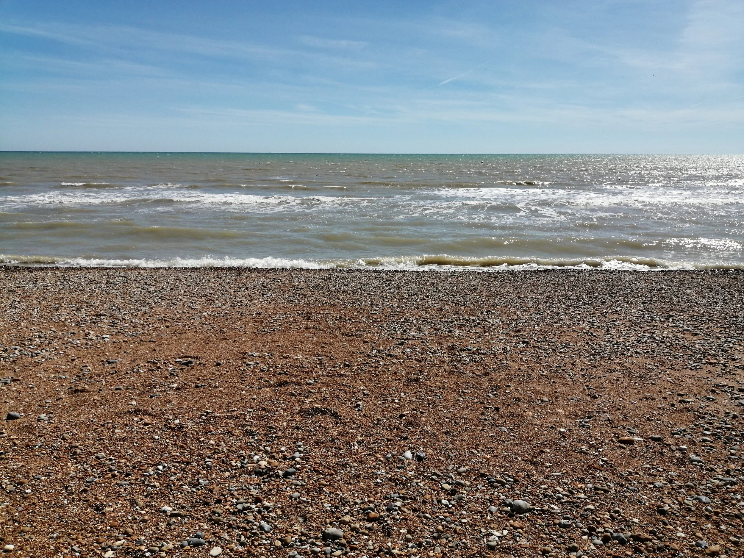 Waves breaking on a pebble and sand beach beneath a blue sky.