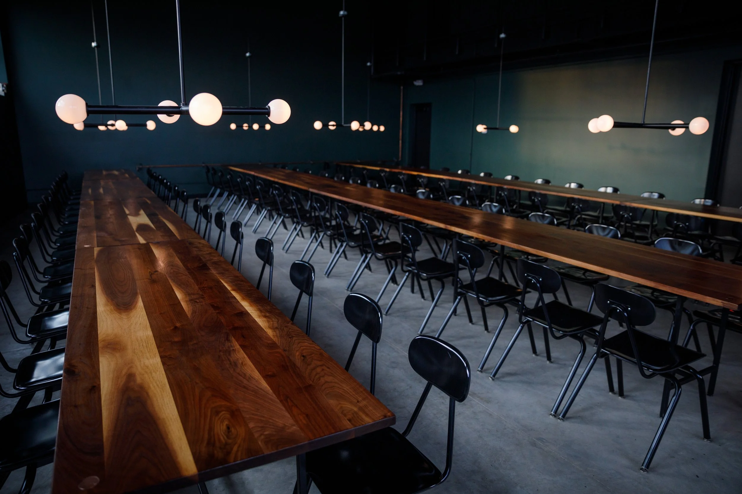 A modern conference room with a long wooden table and black chairs, illuminated by spherical pendant lights hanging from the ceiling.