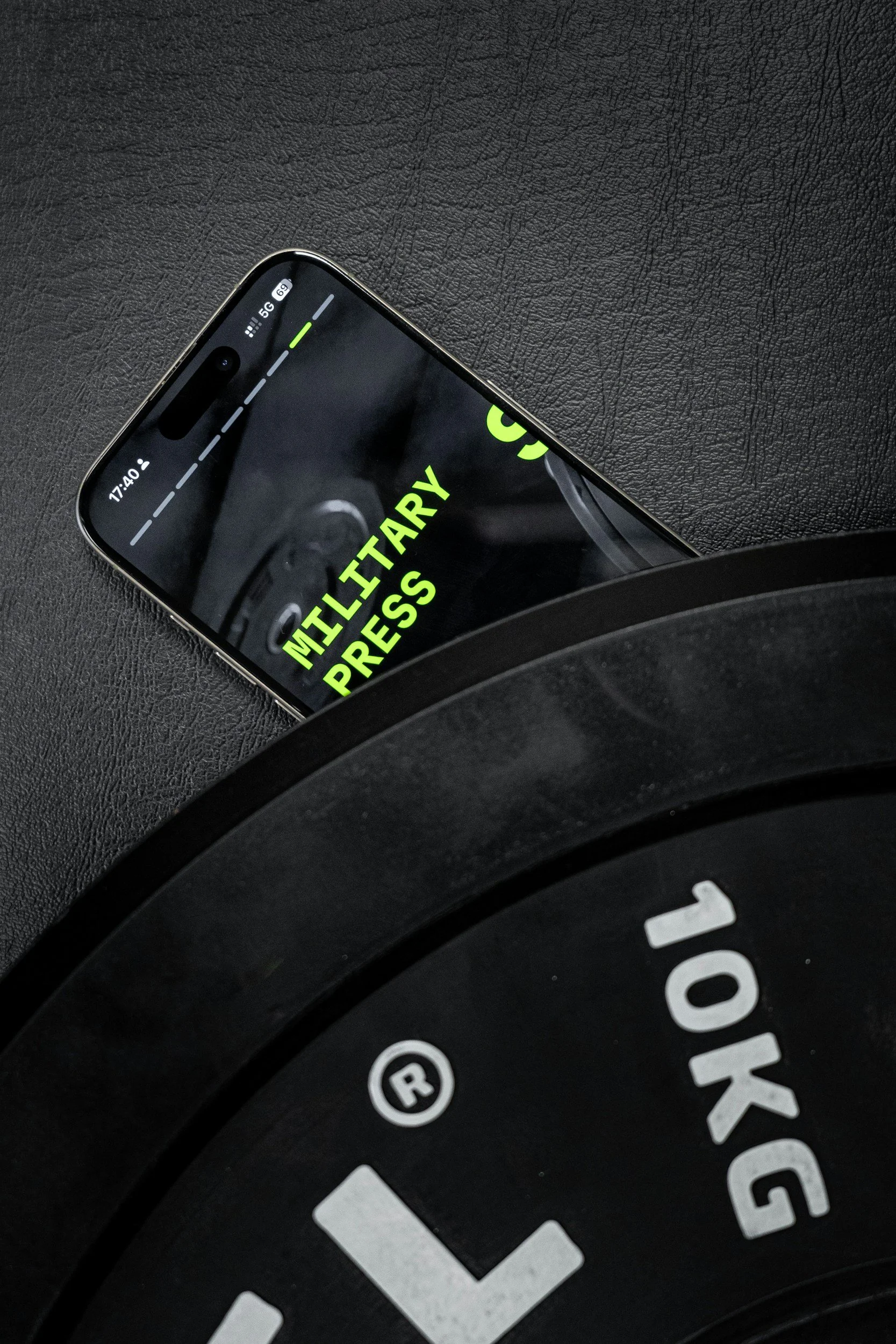 A smartphone displaying a message about pressing the multi-tary button, partially obscured by a black weight plate with the text '10KG' on it, on a black textured surface.