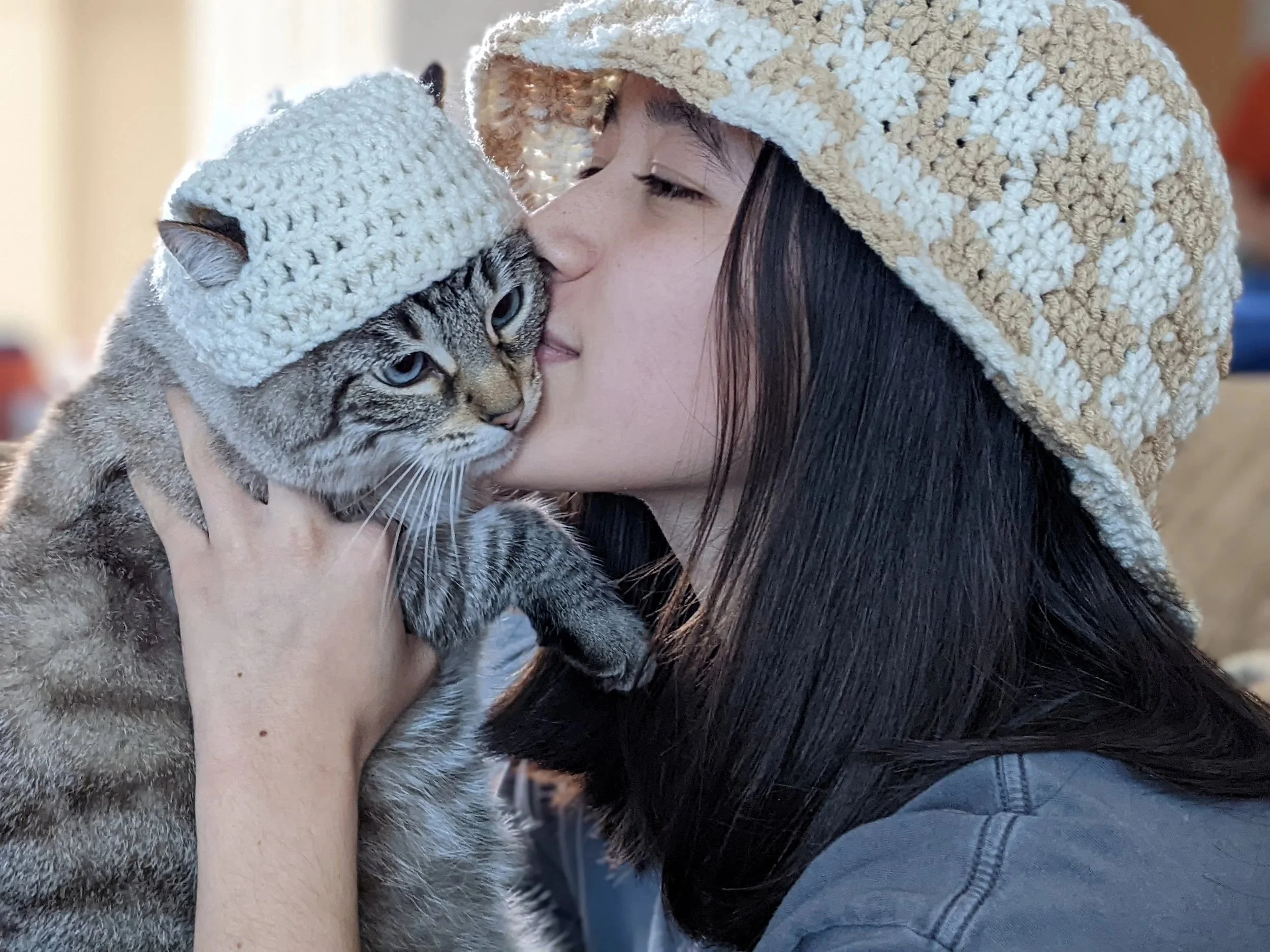 Kyra holding her cat up, kissing her face. Both are wearing matching crochet bucket hats.