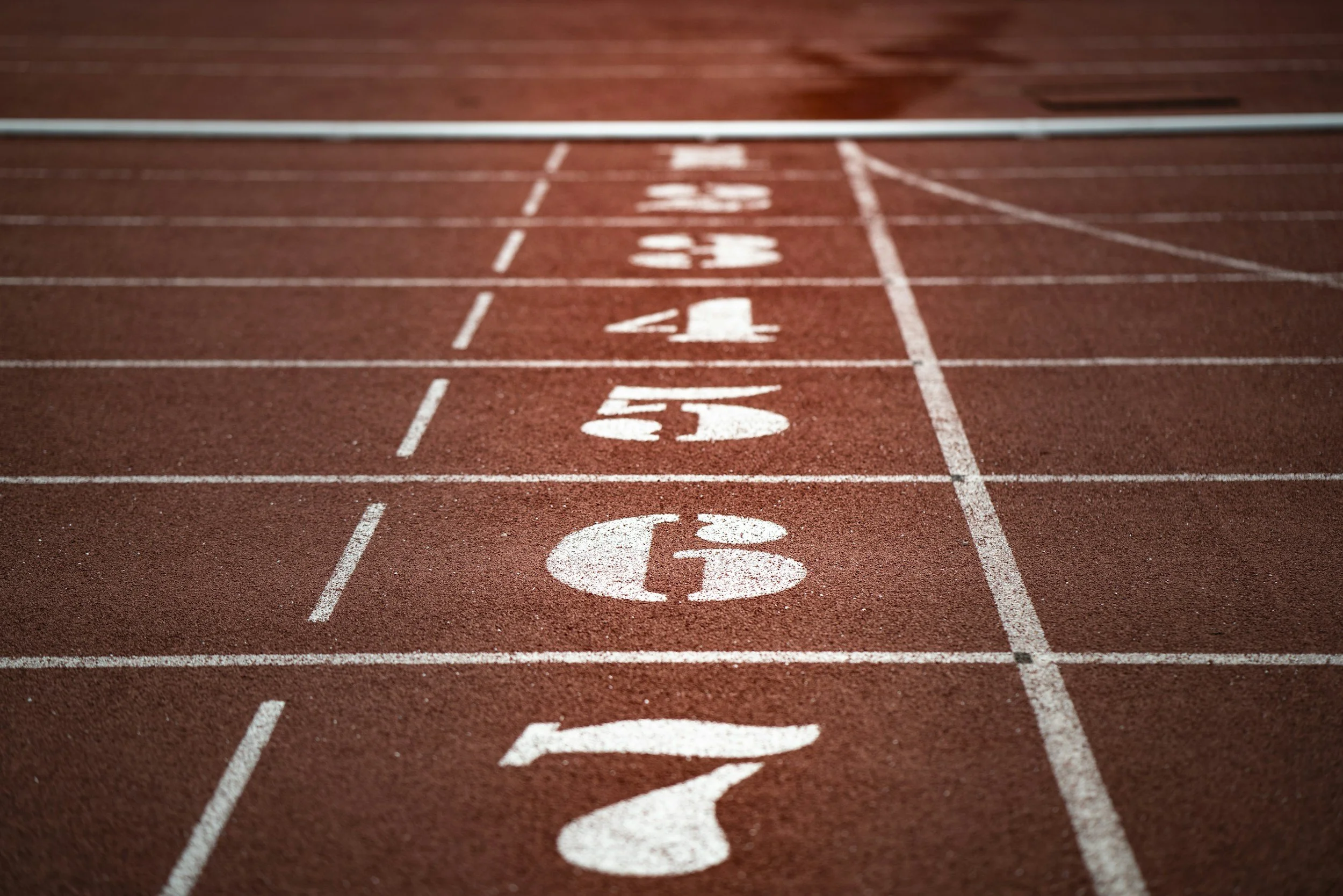 Close-up of a red running track with white lane markings and numbers from 1 to 6.