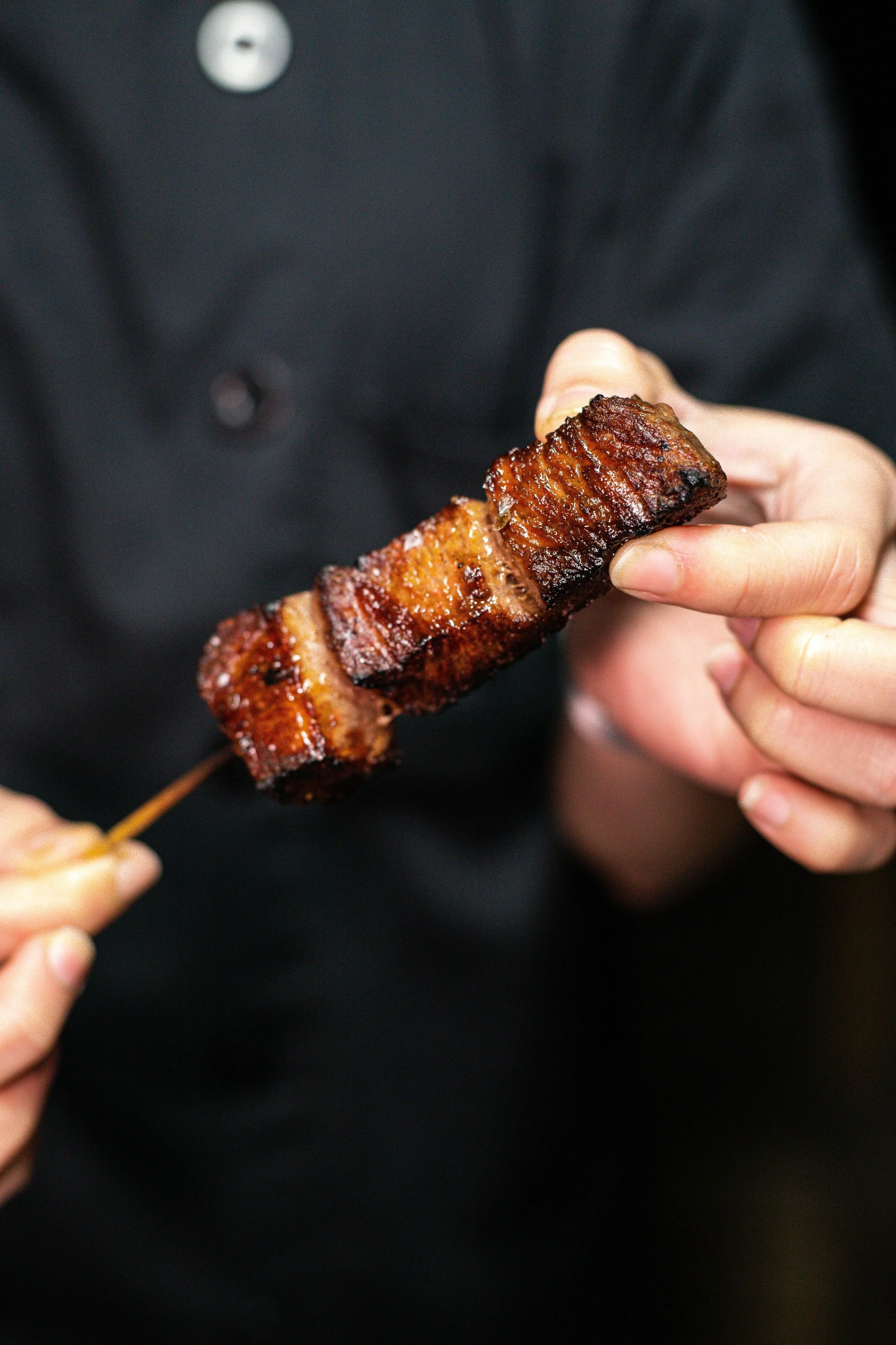Person holding a skewered piece grilled pork belly