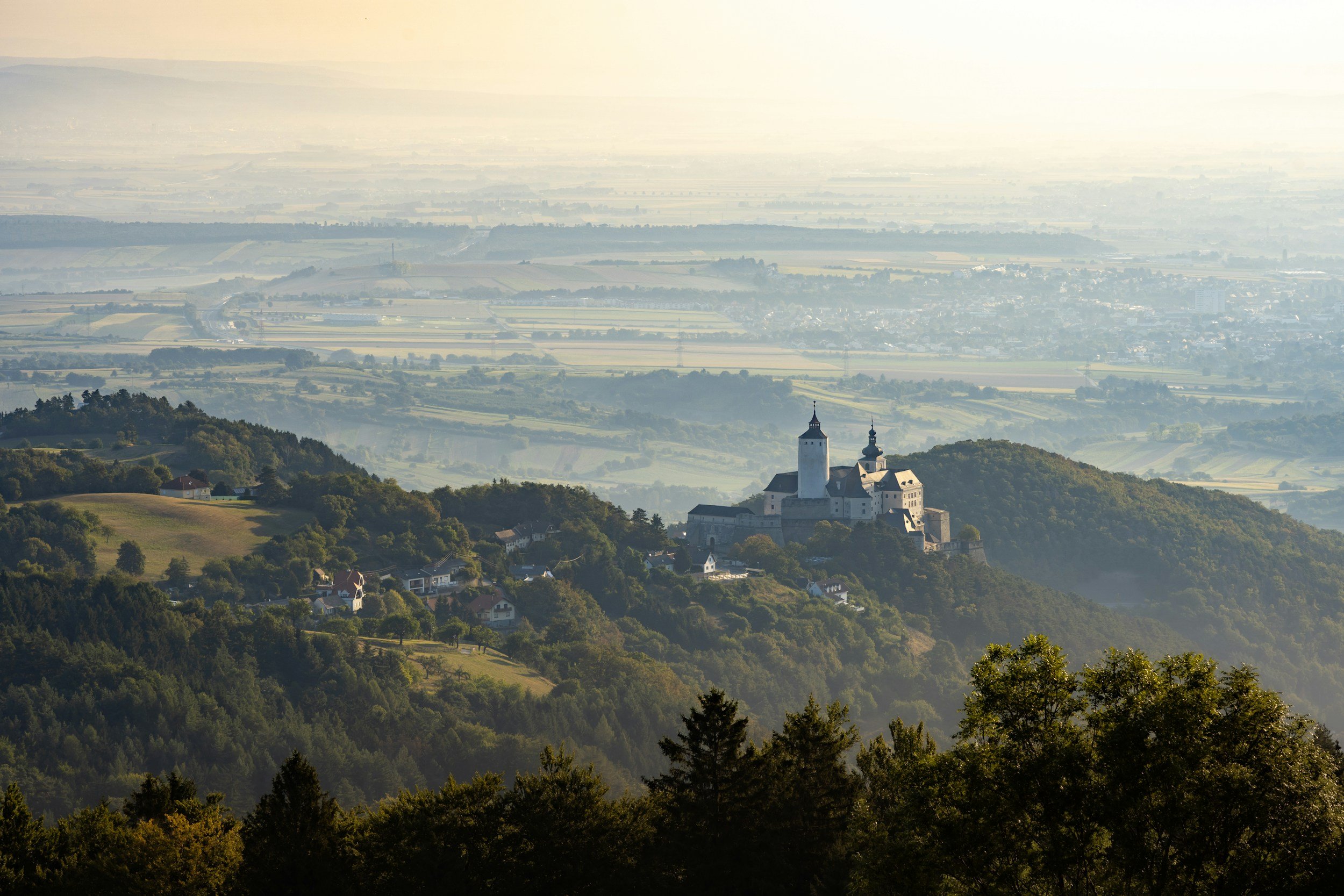 Berg mit Schloss und umgebender Landschaft, im Hintergrund weite Ebenen und Felder.