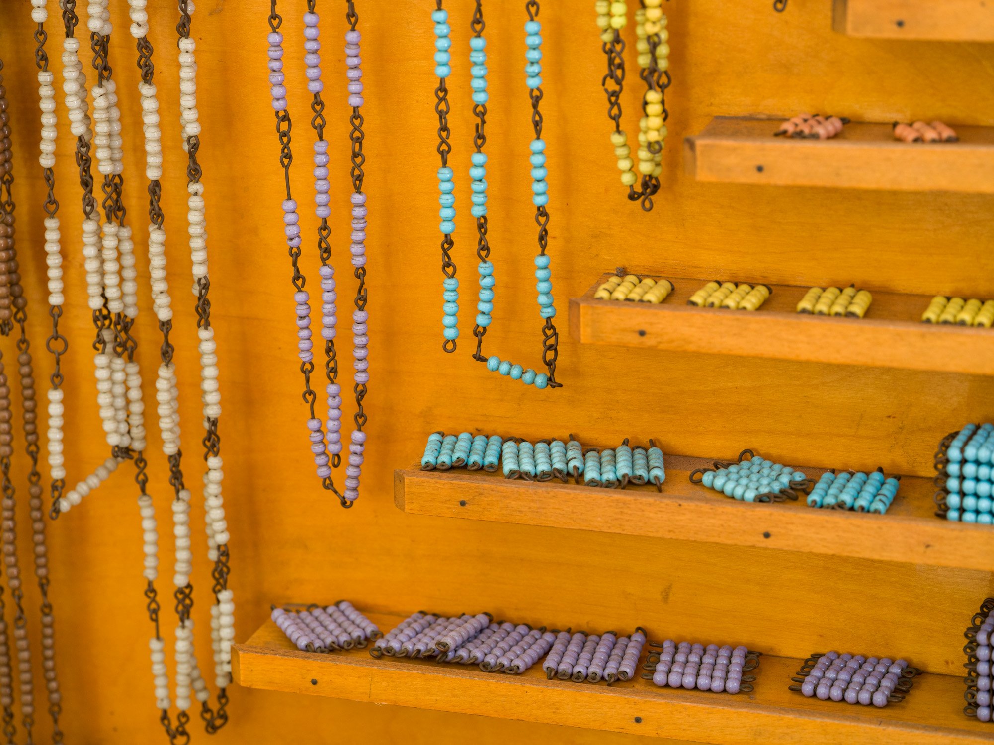 Colorful beaded jewelry hanging on wooden display shelves with beads arranged on the shelves.