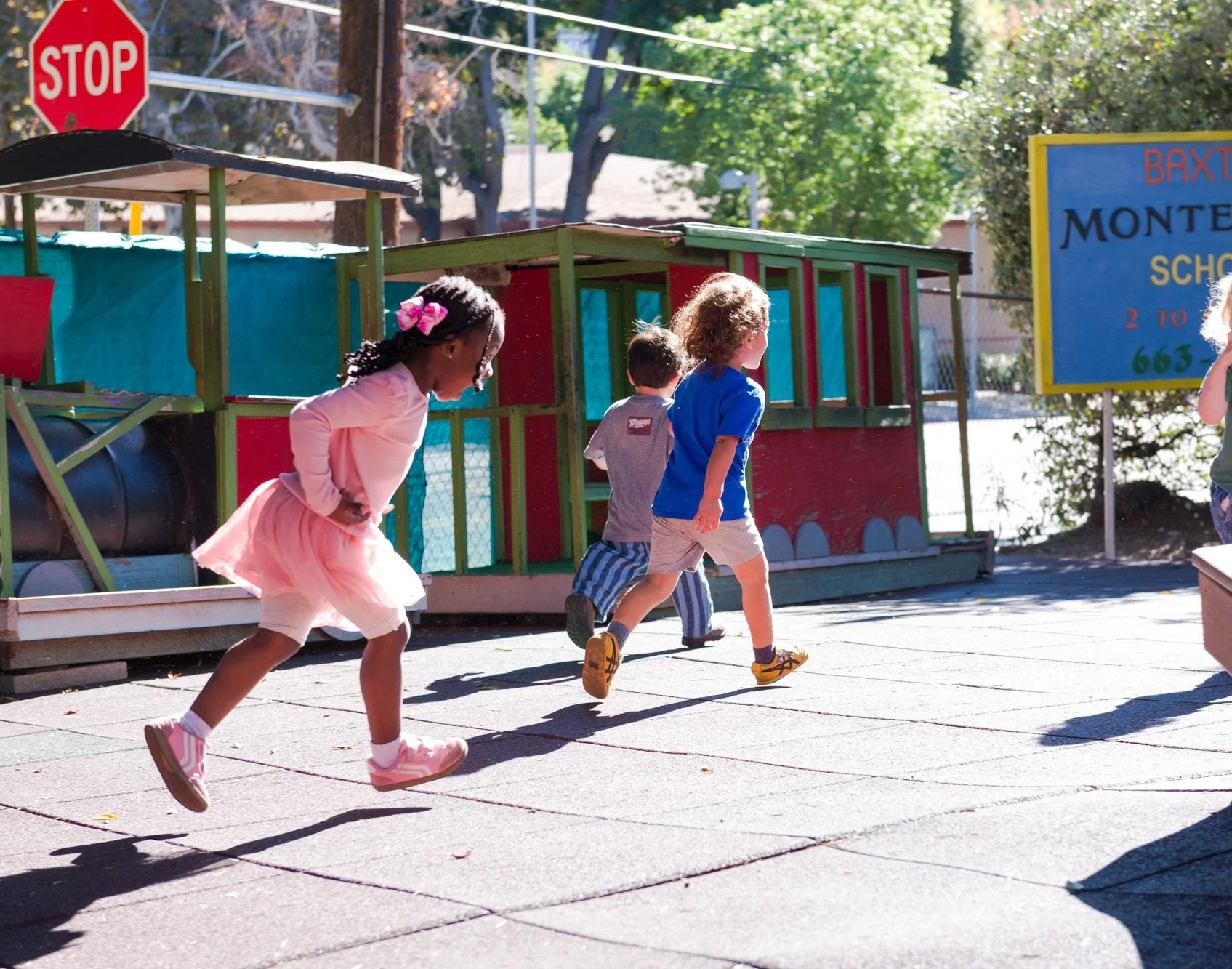 Children running and playing outside on a sidewalk near a school playground.