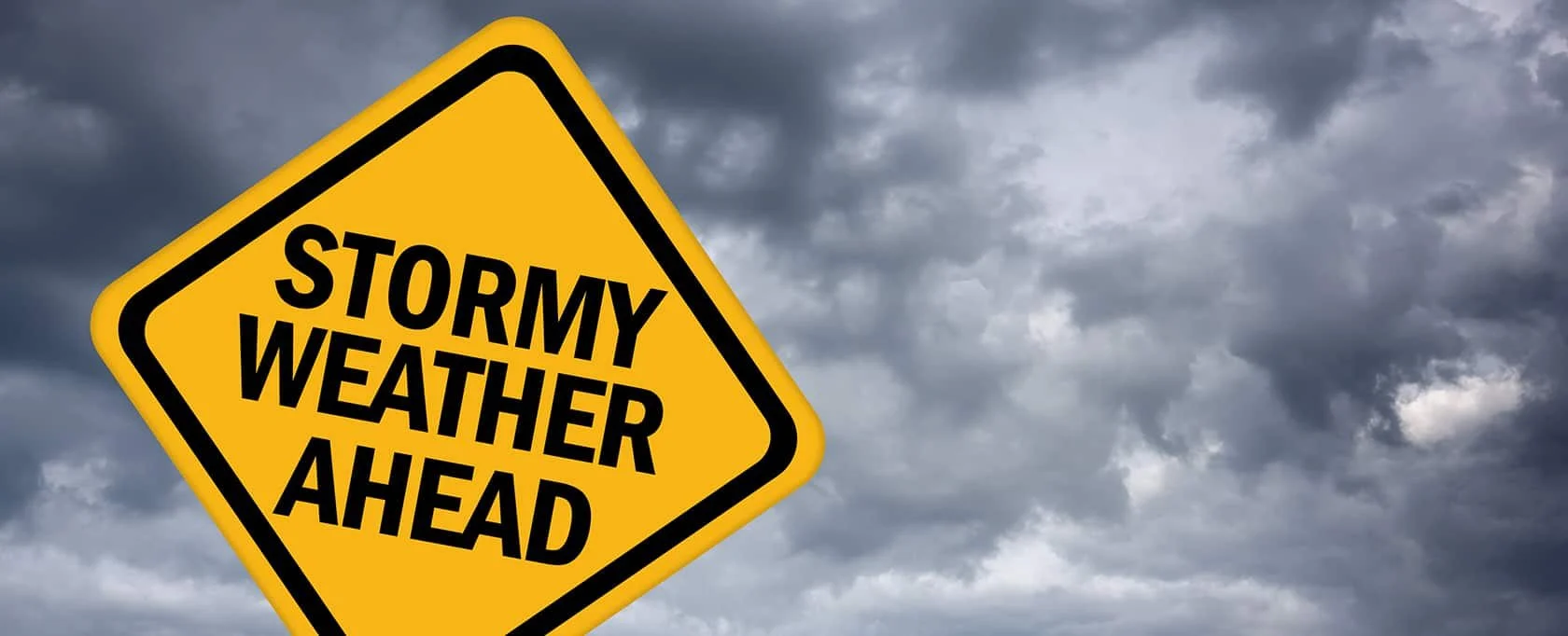 Yellow stormy weather ahead road sign against dark storm clouds, representing hurricane season preparation in Gainesville, FL