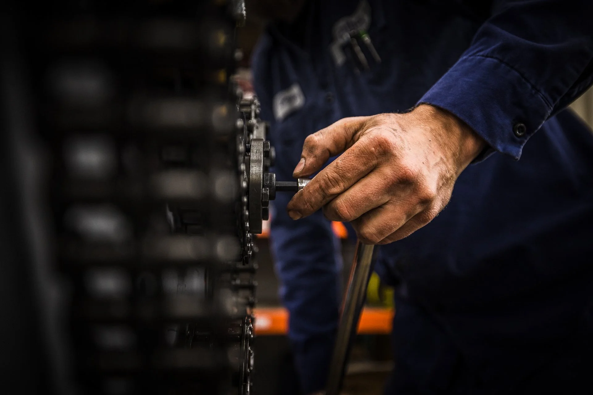 A person's hand using a wrench on a mechanical device or machinery in a workshop or industrial setting