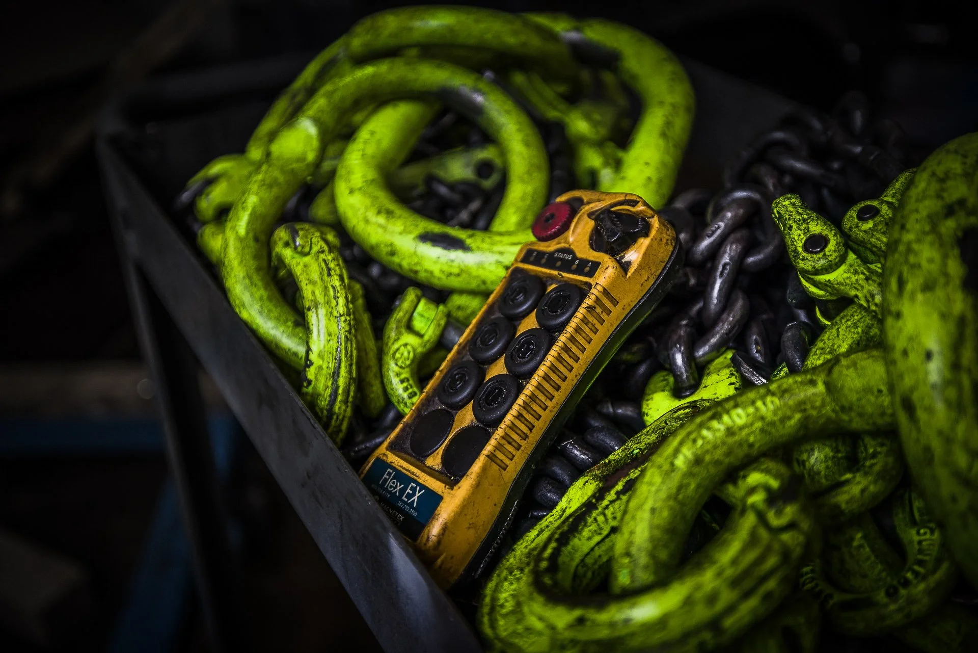 Heavy-duty chains, some yellow and some black, inside a black container with a remote control placed on top.