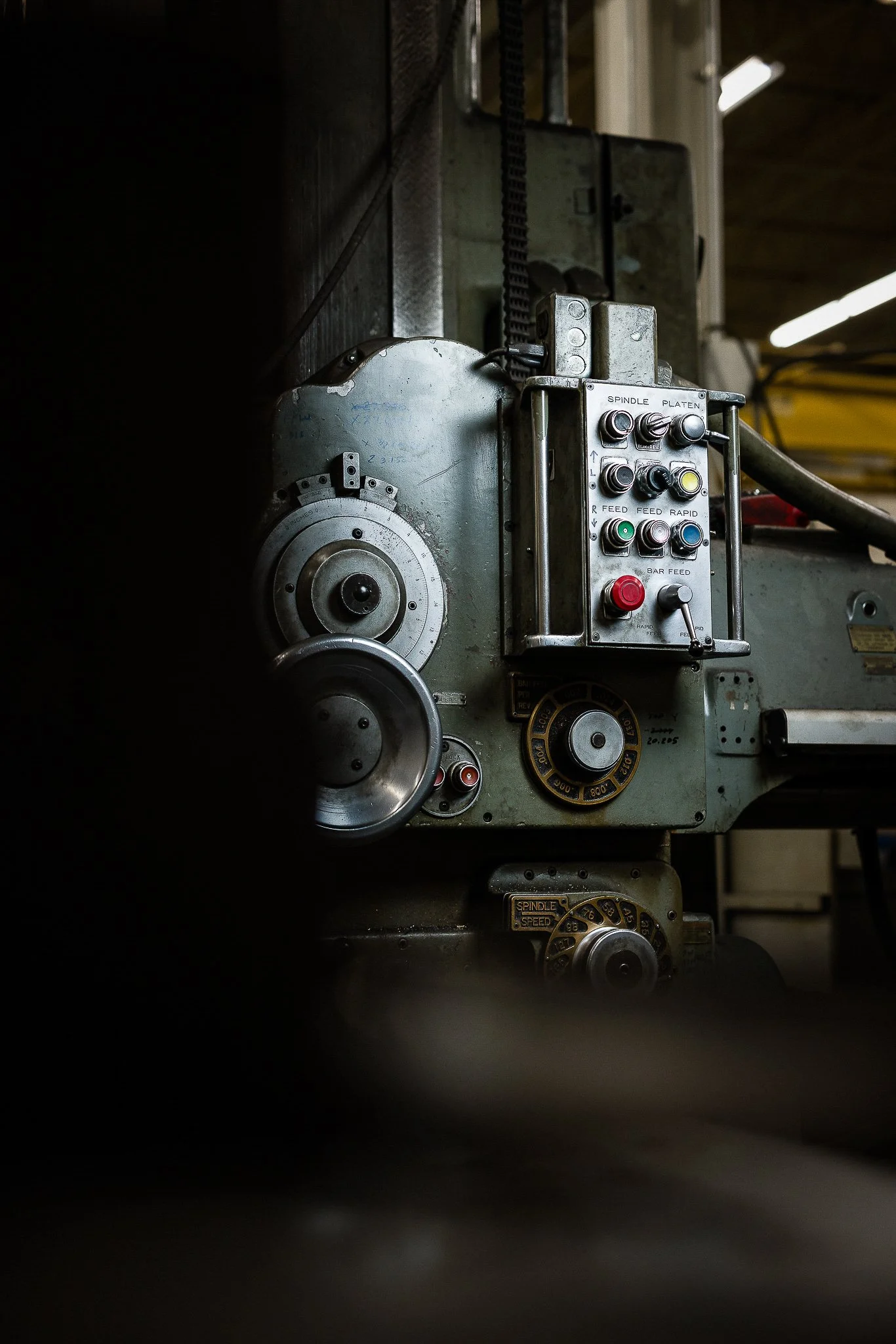 Close-up of vintage industrial machine with control panel, knobs, and dials, partially lit in a dim workshop environment.