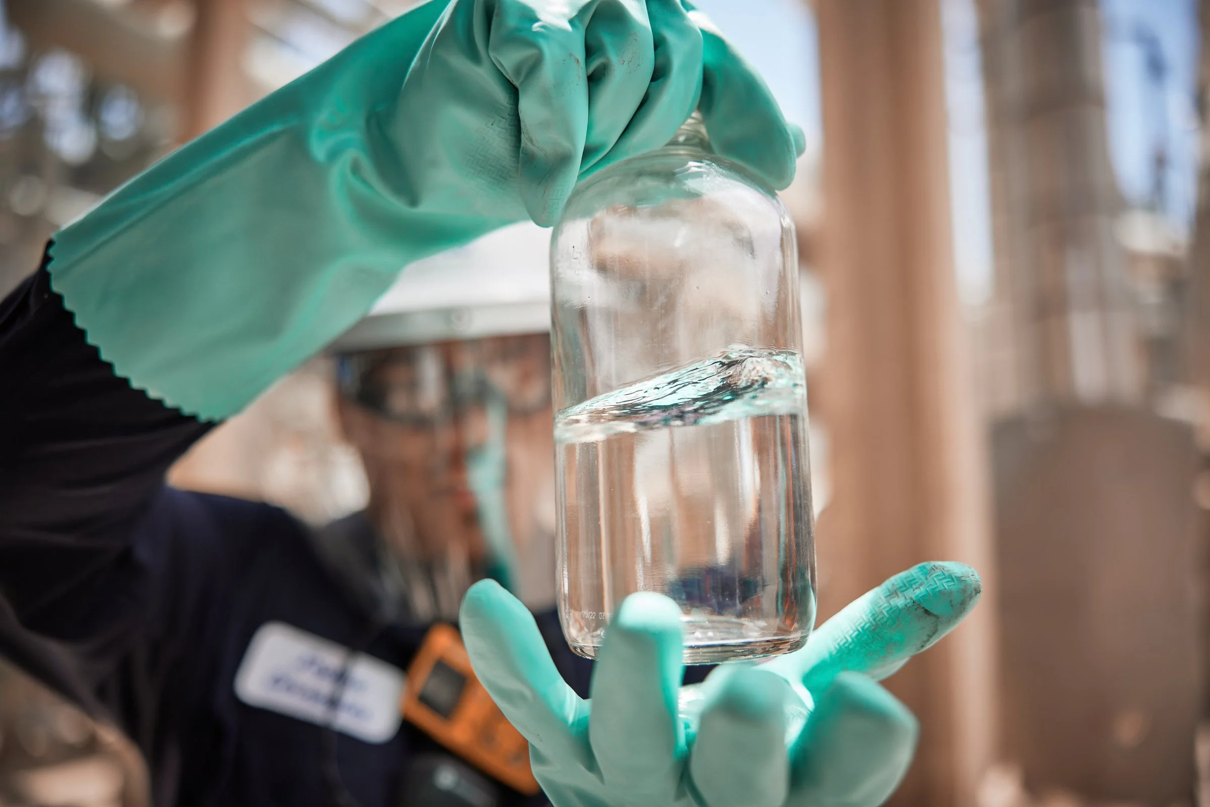 Person wearing green gloves holding a glass jar filled with water.