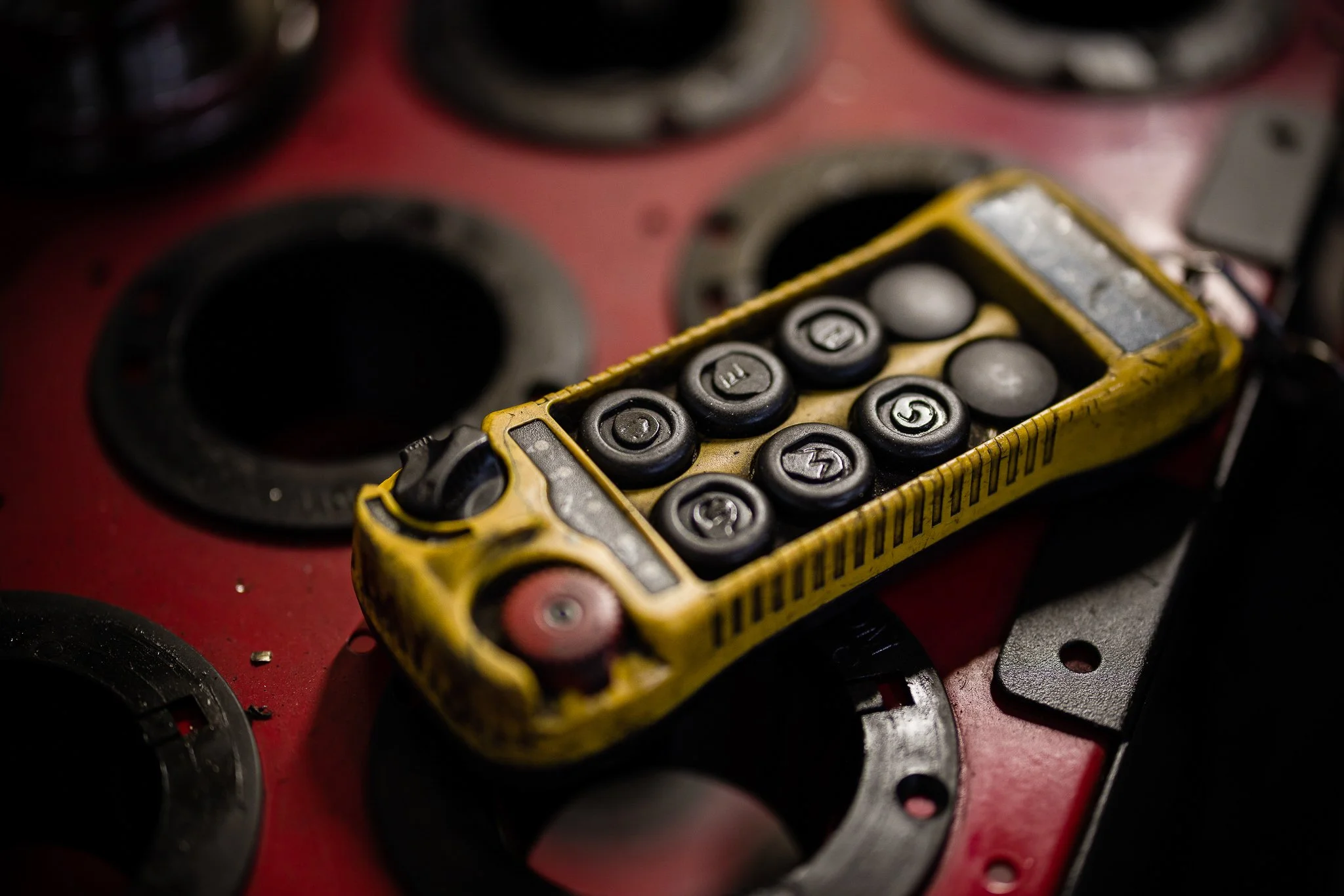 Close-up of a yellow vintage remote control with black buttons numbered 1 through 9, resting on a red surface with circular cutouts and metallic components.