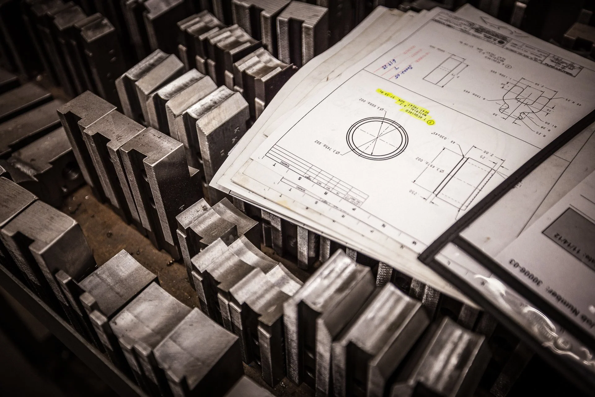 Technical drawings and blueprints resting on metal molds or dies in an industrial setting.