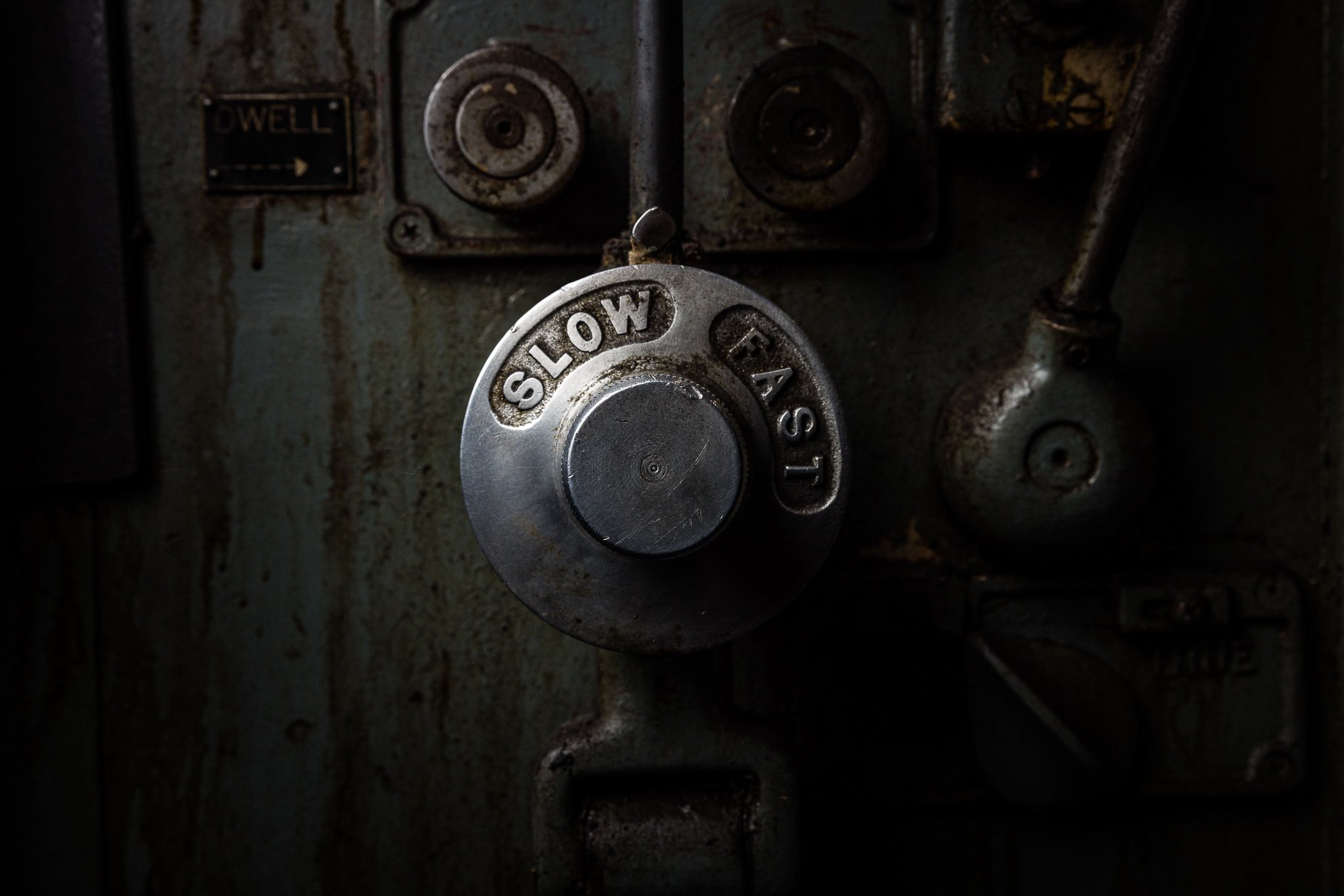 Close-up of a metal control knob with the words "SLOW" and "FAST" engraved on it, mounted on a dark, industrial panel.