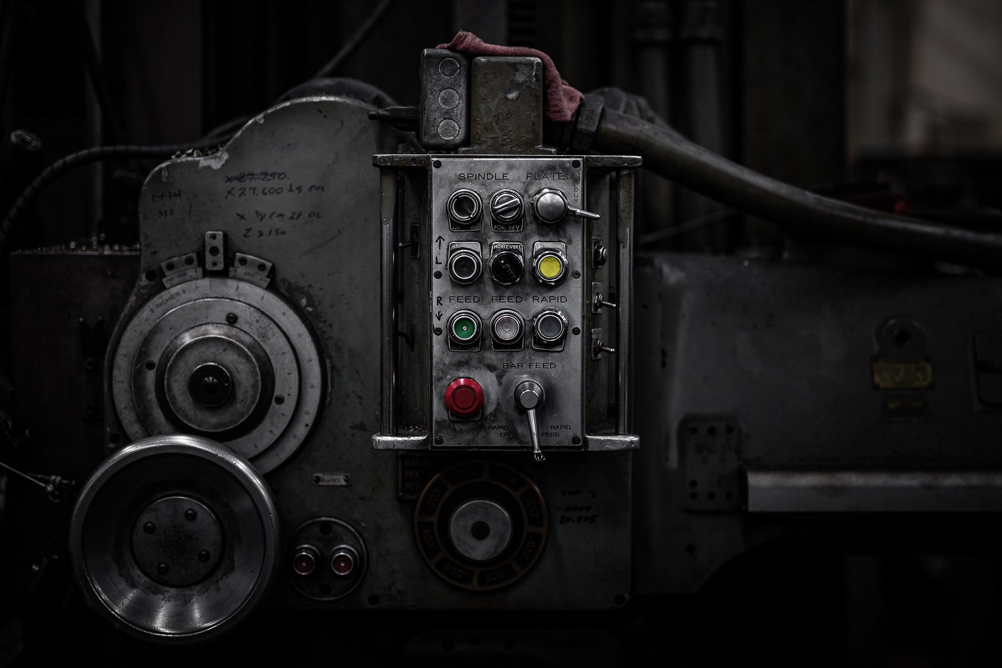 Close-up of industrial machine control panel with various buttons, switches, and dials, some with labels like 'feed' and 'rapid'. The surface is metallic and shows signs of wear.