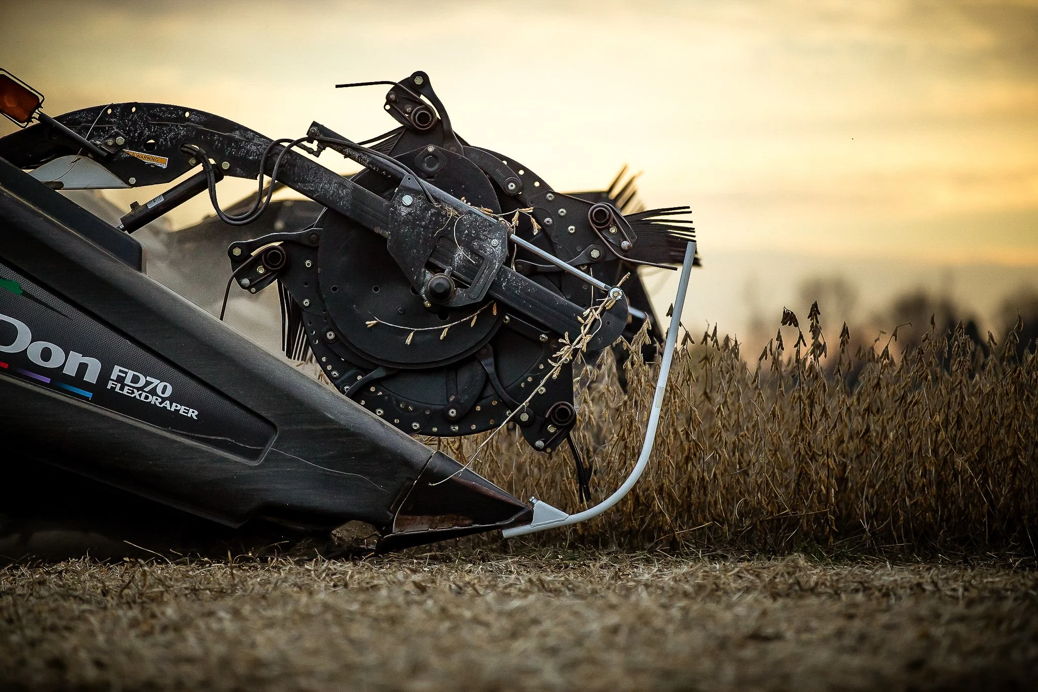 Close-up of a corn harvester machine working in a field at sunset.
