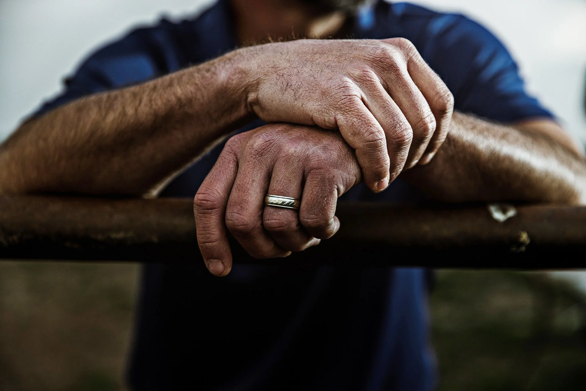 Close-up of a person's clasped hands resting on a wooden surface, showing a wedding band on their ring finger.