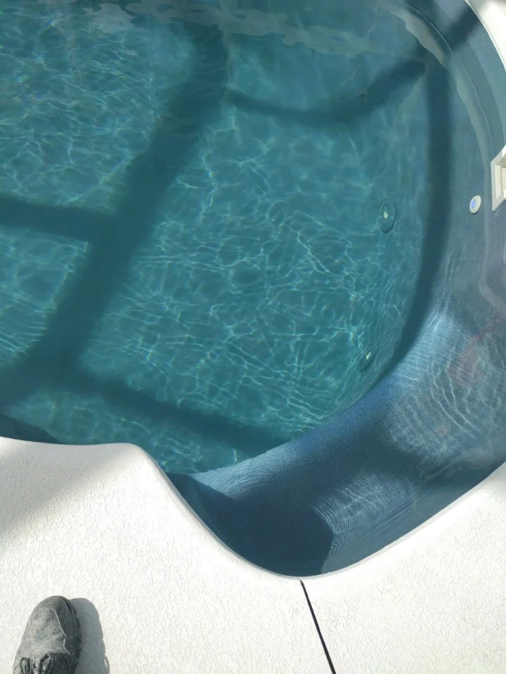 Close-up of a hot tub filled with water, showing the interior and part of the surrounding white deck with a person's shoe visible.