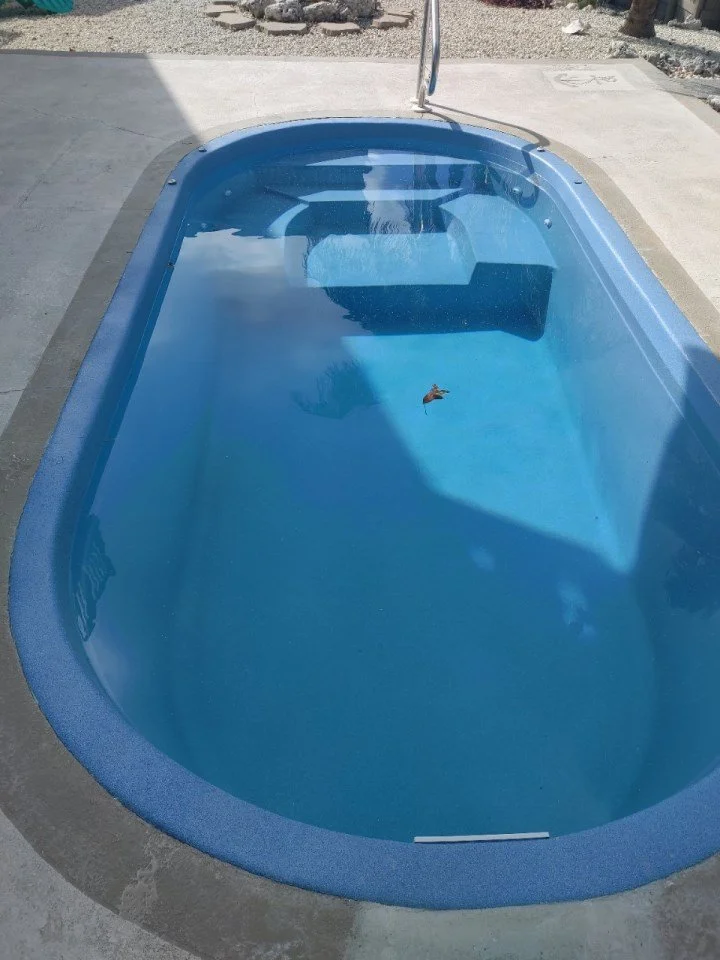 Empty blue hot tub with a small leaf floating inside, outdoors on a concrete surface.