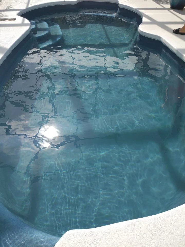 An empty hot tub filled with clear water on an outdoor pool deck with sunlight reflecting on its surface.