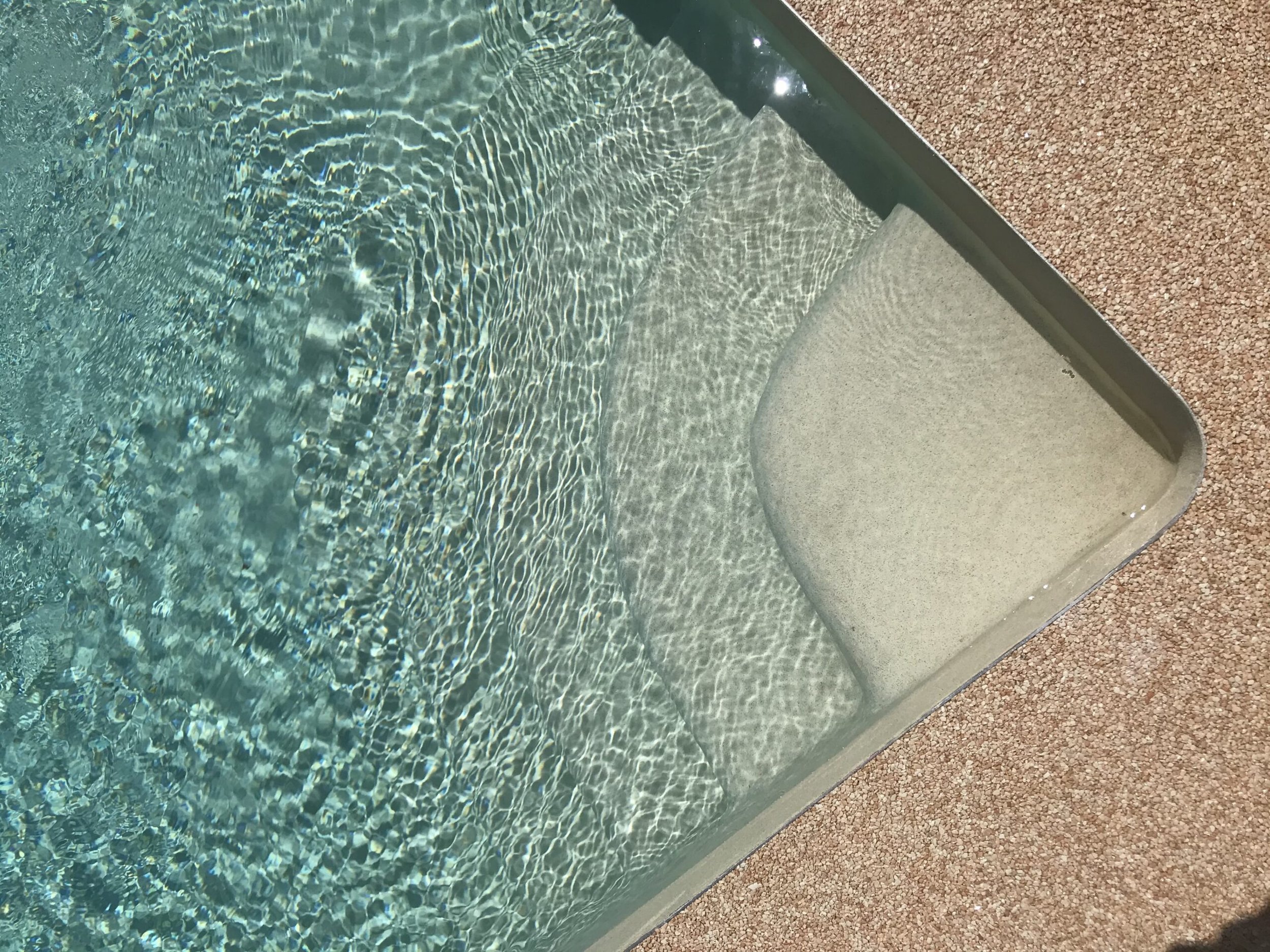 Empty outdoor pool with water and a concrete step, surrounded by textured concrete pavement.