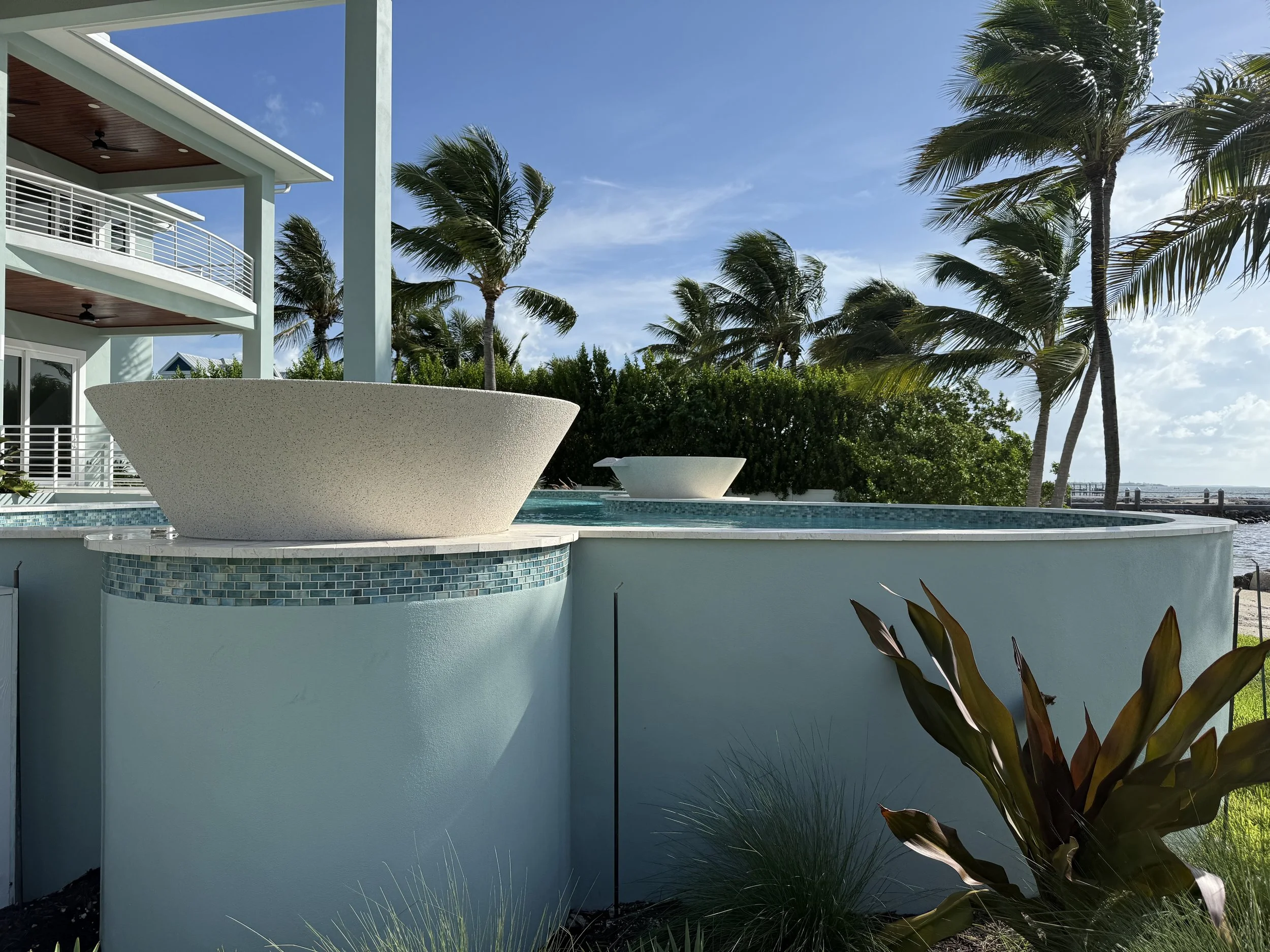 Modern house with outdoor pool surrounded by palm trees under a blue sky.