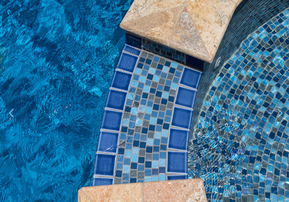 Close-up of a swimming pool with blue mosaic tiles, stone coping, and water ripples.
