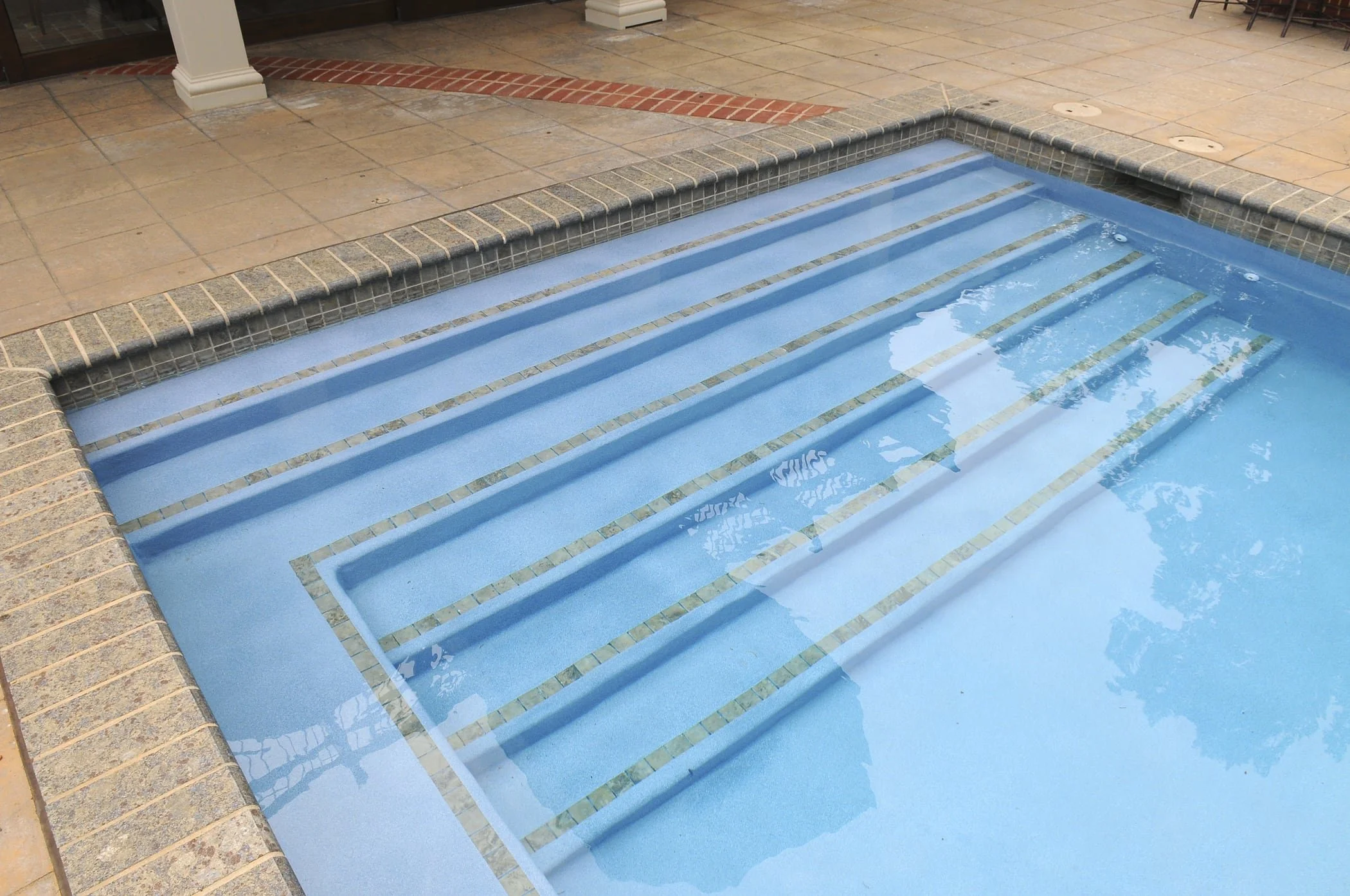 Indoor swimming pool with tiled steps leading into the water and tan tiled surrounding area.