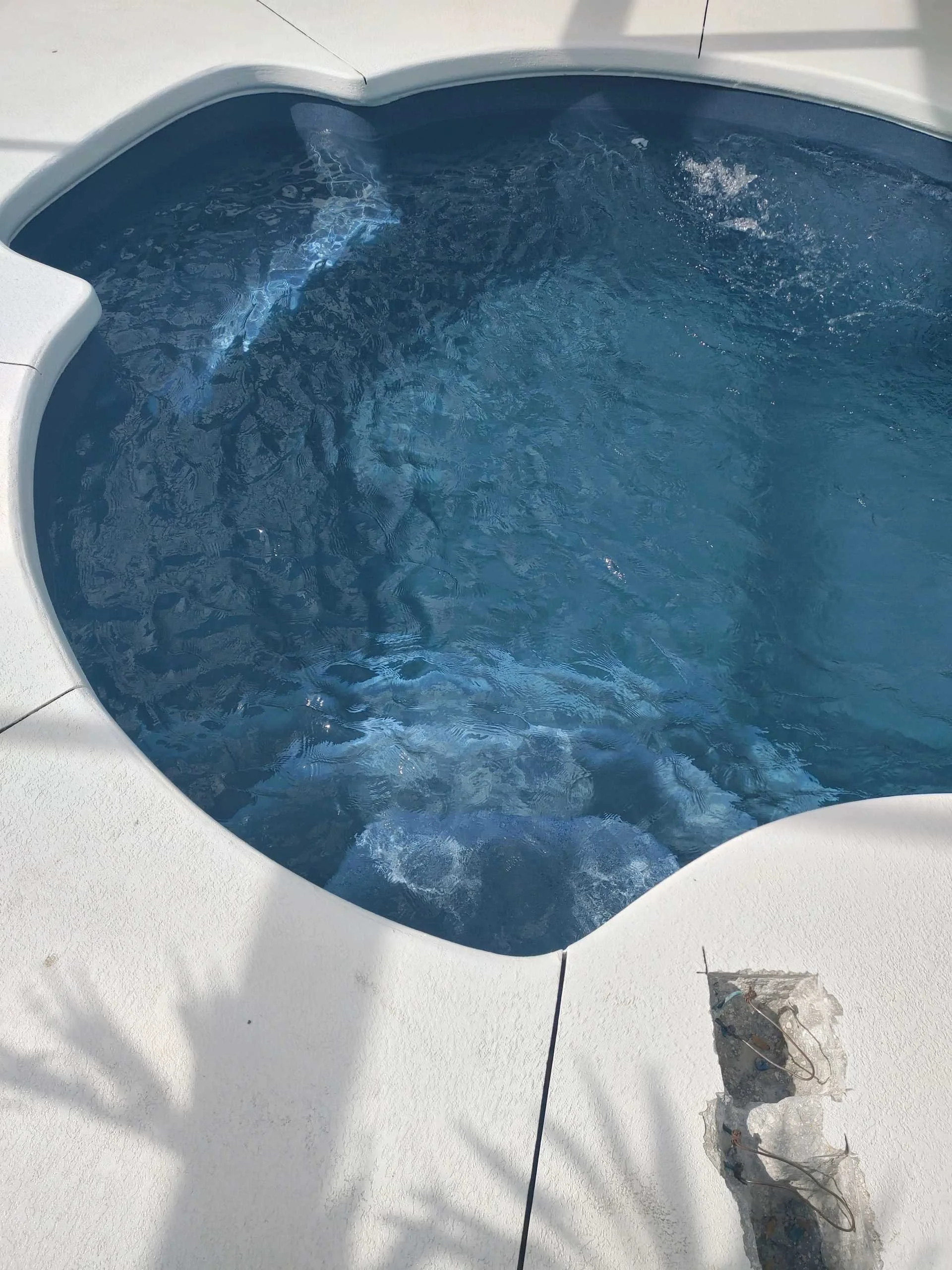 A round hot tub filled with blue water, located on a white deck, with a damaged section of the deck visible in the foreground.