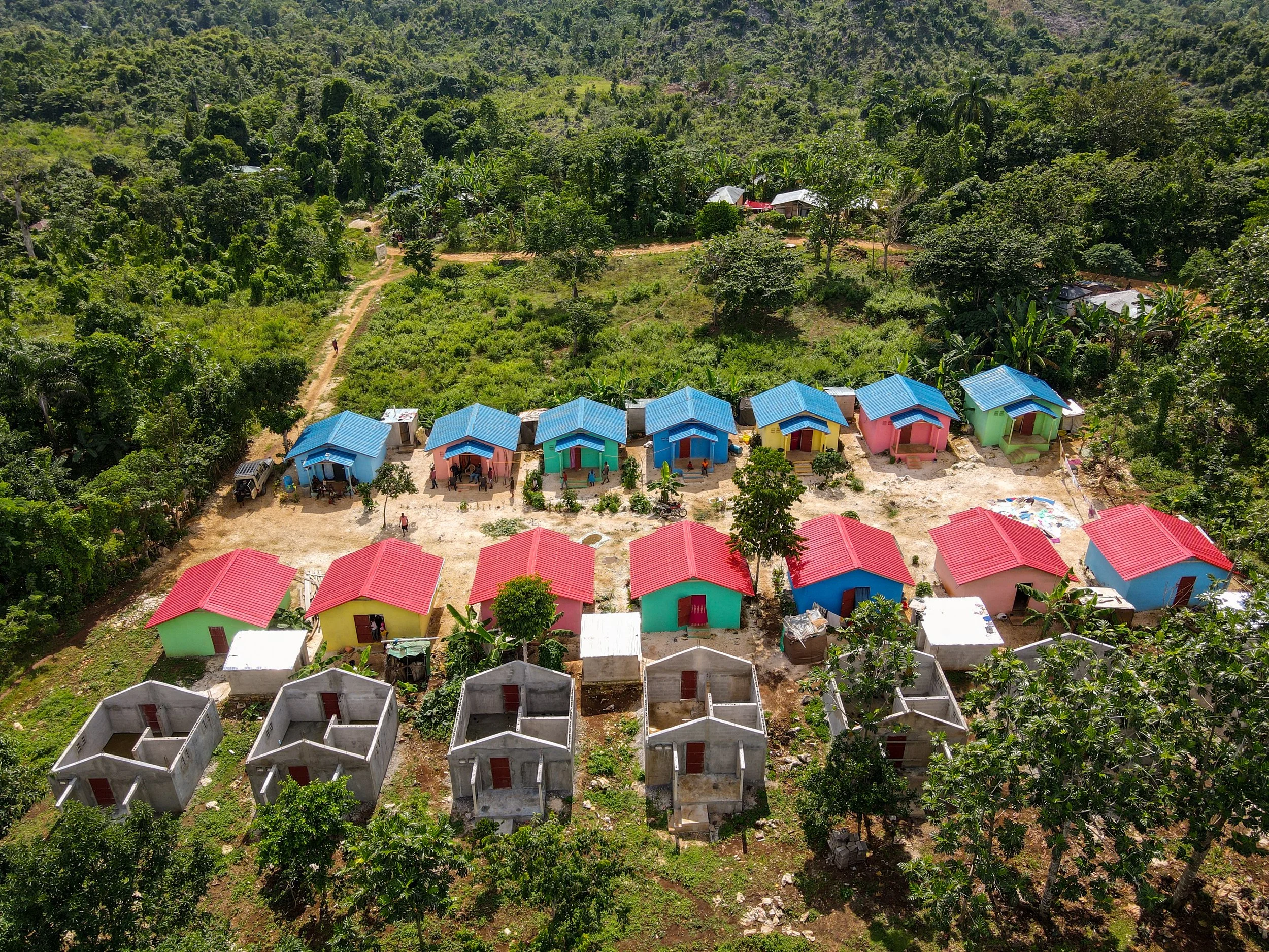 Colorful small houses with red, green, pink, and blue roofs in a rural area surrounded by green trees and vegetation.