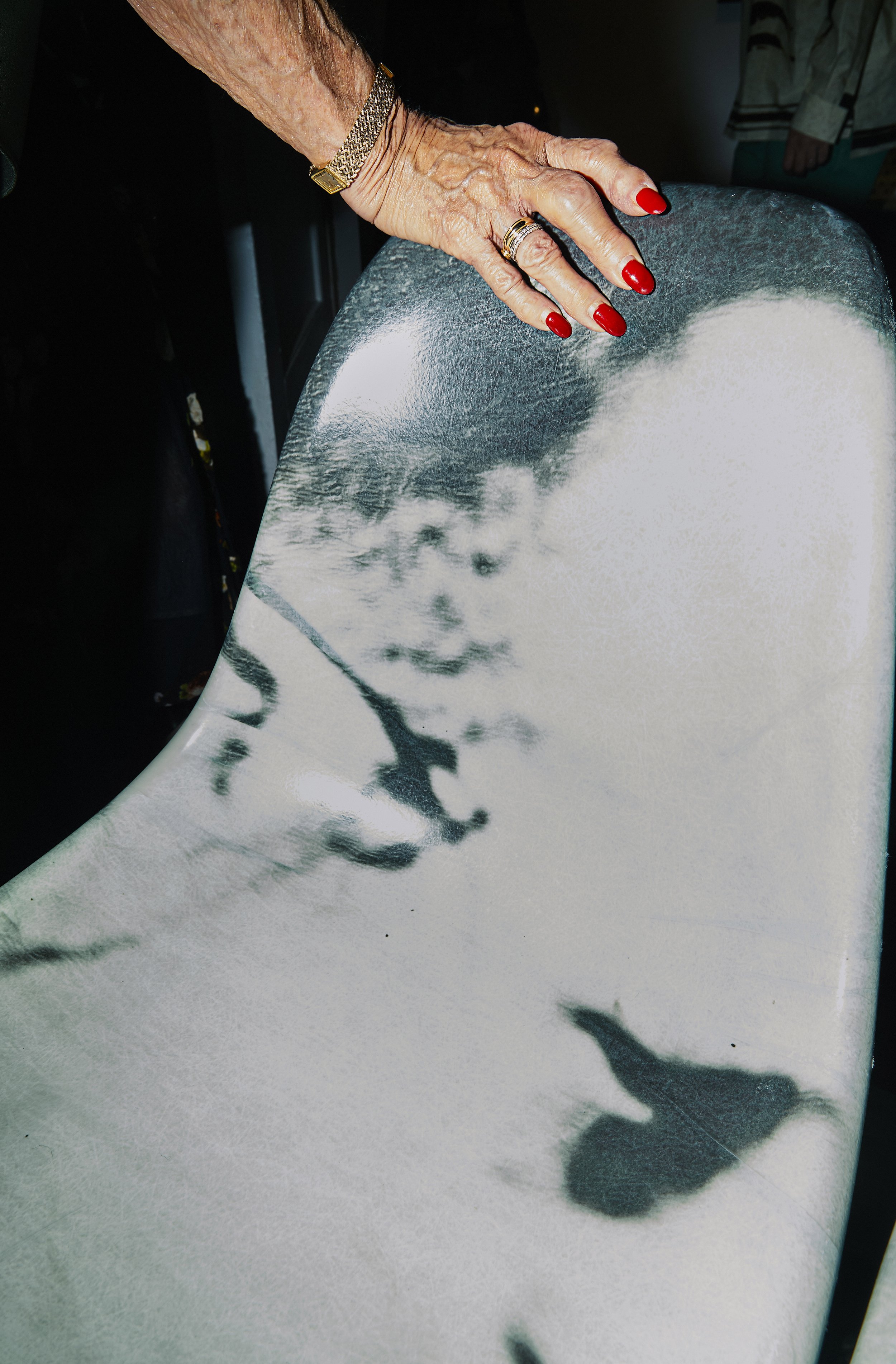 A person's hand with red painted nails, jewelry, and rings, resting on a surface with photo projections of a young child's face and butterflies.