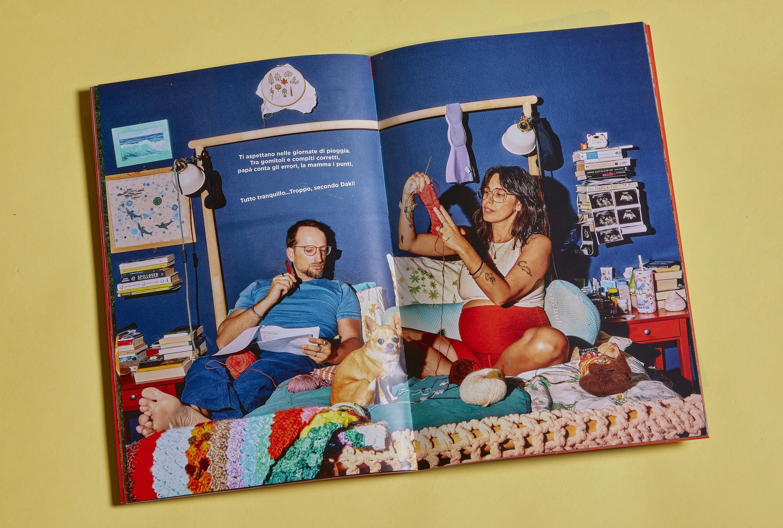 A family storybook open showing documentary photography of an expecting couple relaxing on a bed with their dog in a domestic interior, photographed for a family storybook.