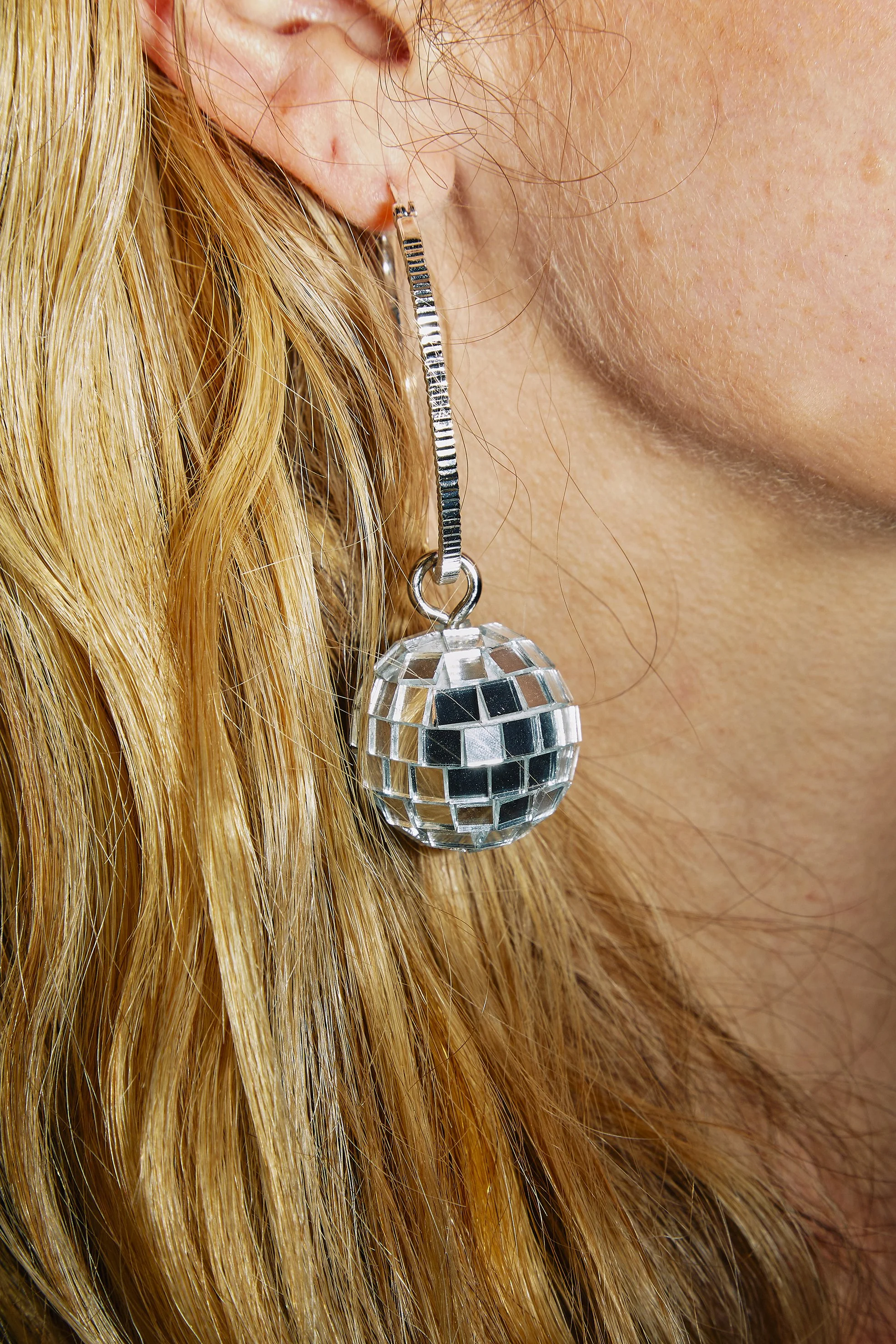 Close-up of a woman's ear with a large, reflective disco ball earring hanging from a silver hook.