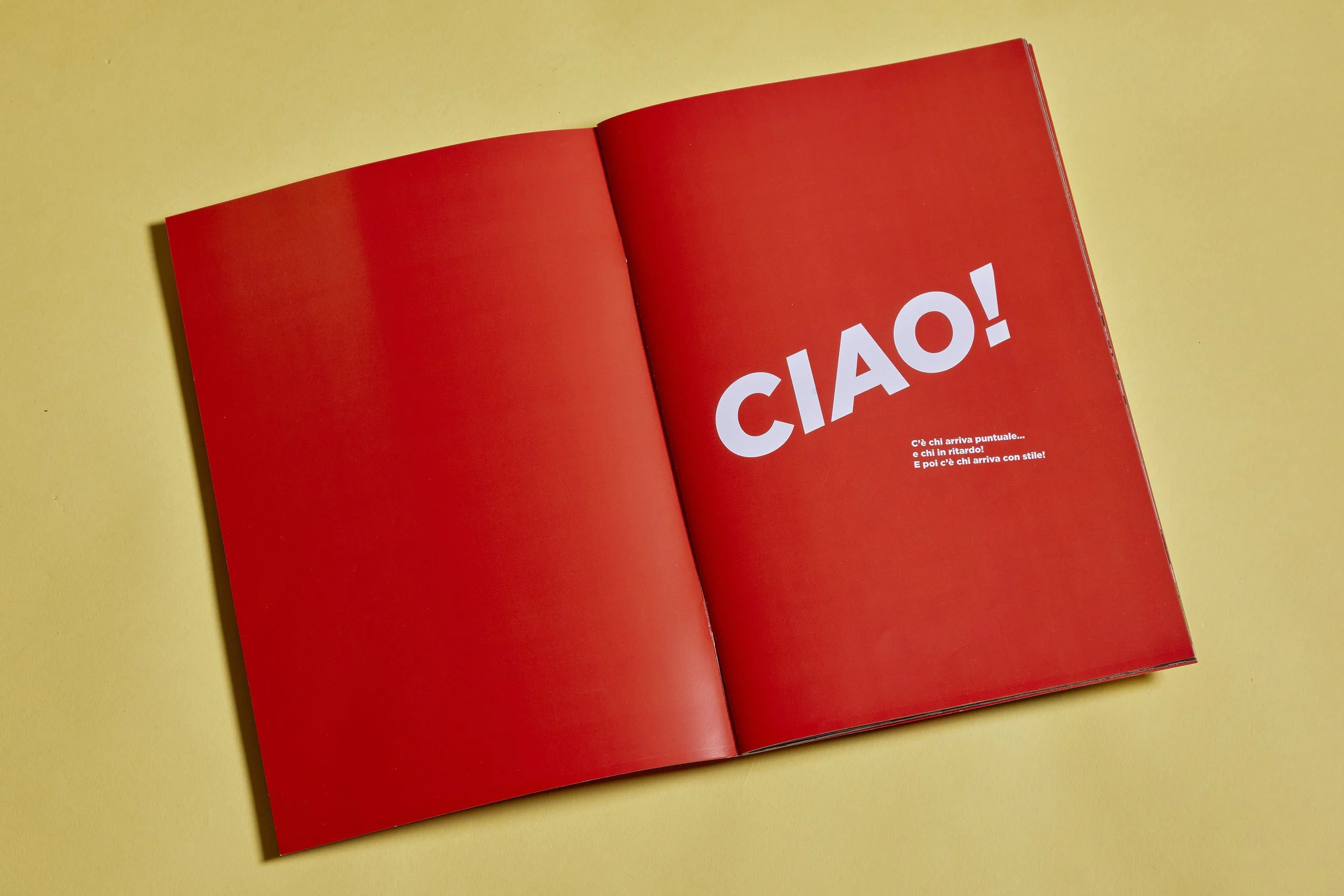 Editorial photography of a printed family photo book open on a red title spread reading “CIAO!”, photographed on a yellow background.