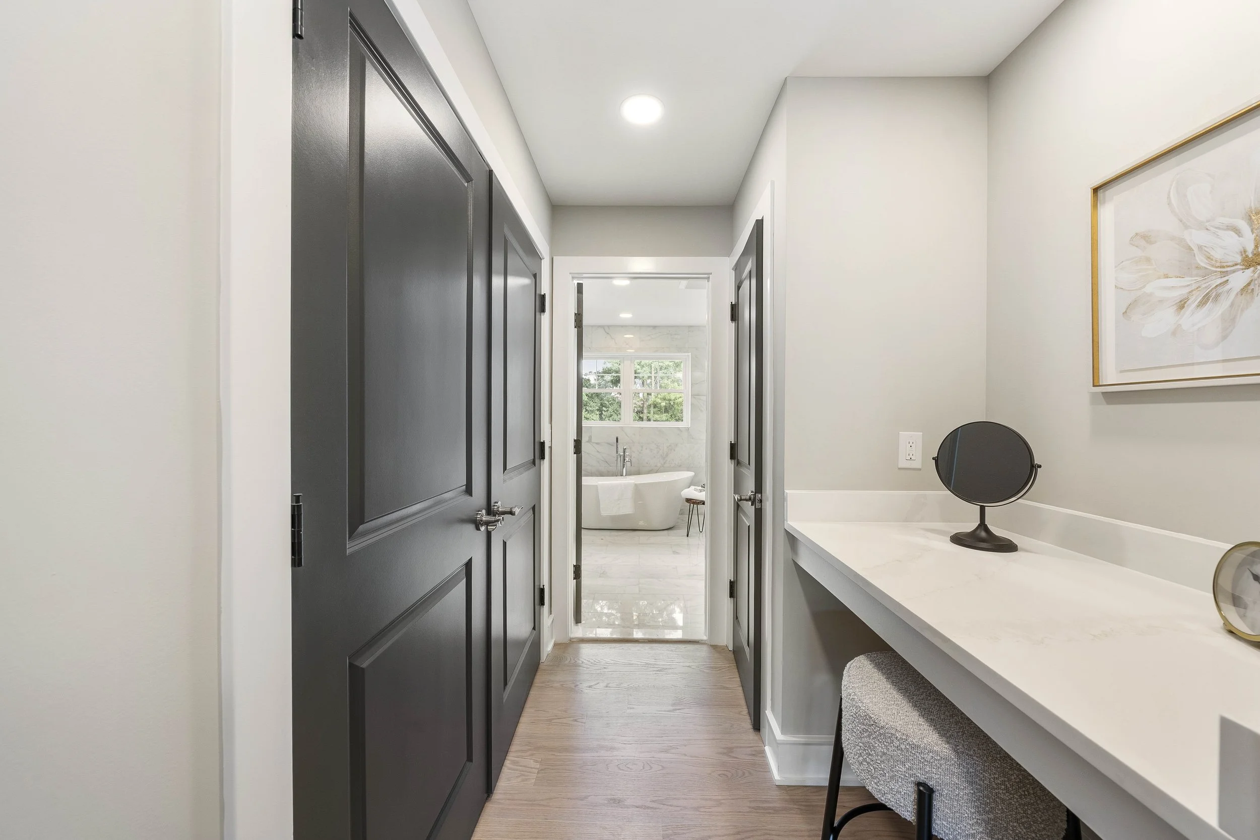 A hallway leading to a bathroom with a freestanding bathtub, two large windows, and a tree view outside.