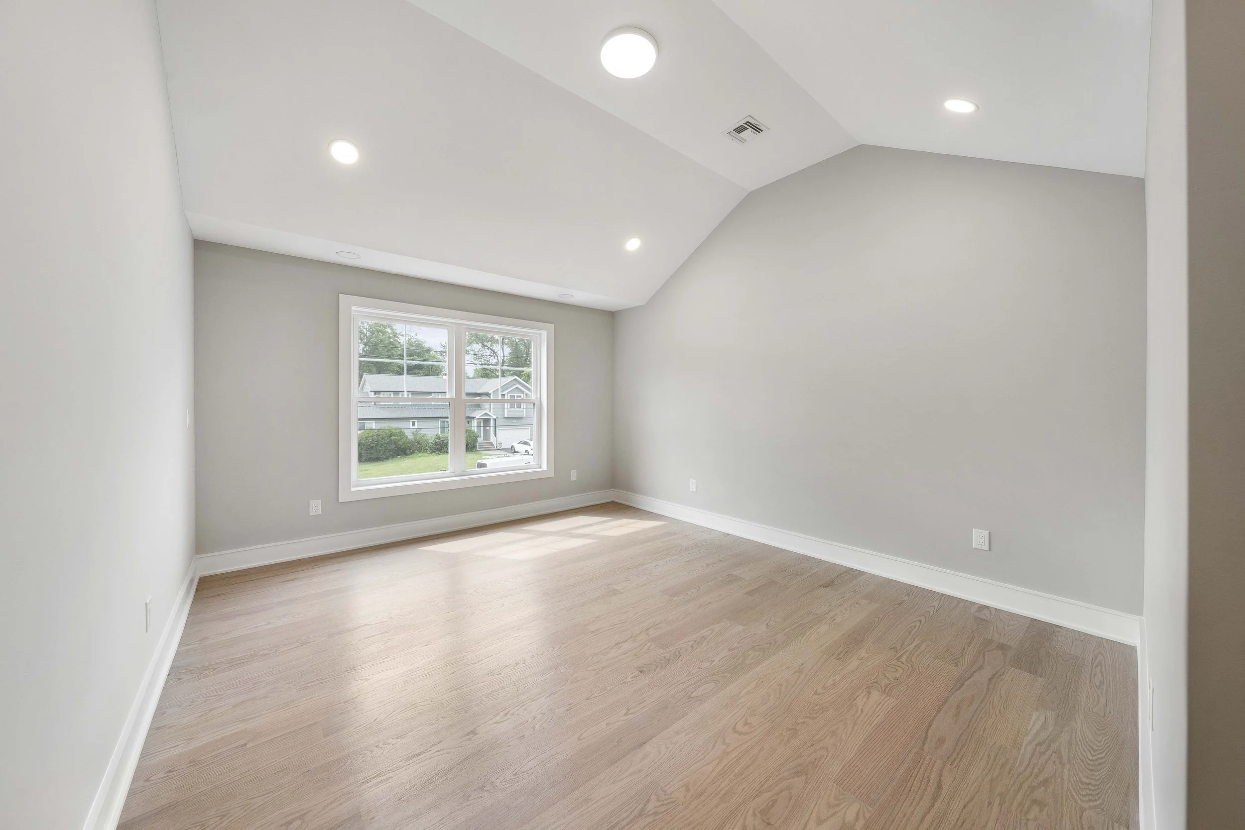 Empty room with hardwood floors, large window, white walls, and ceiling lights.