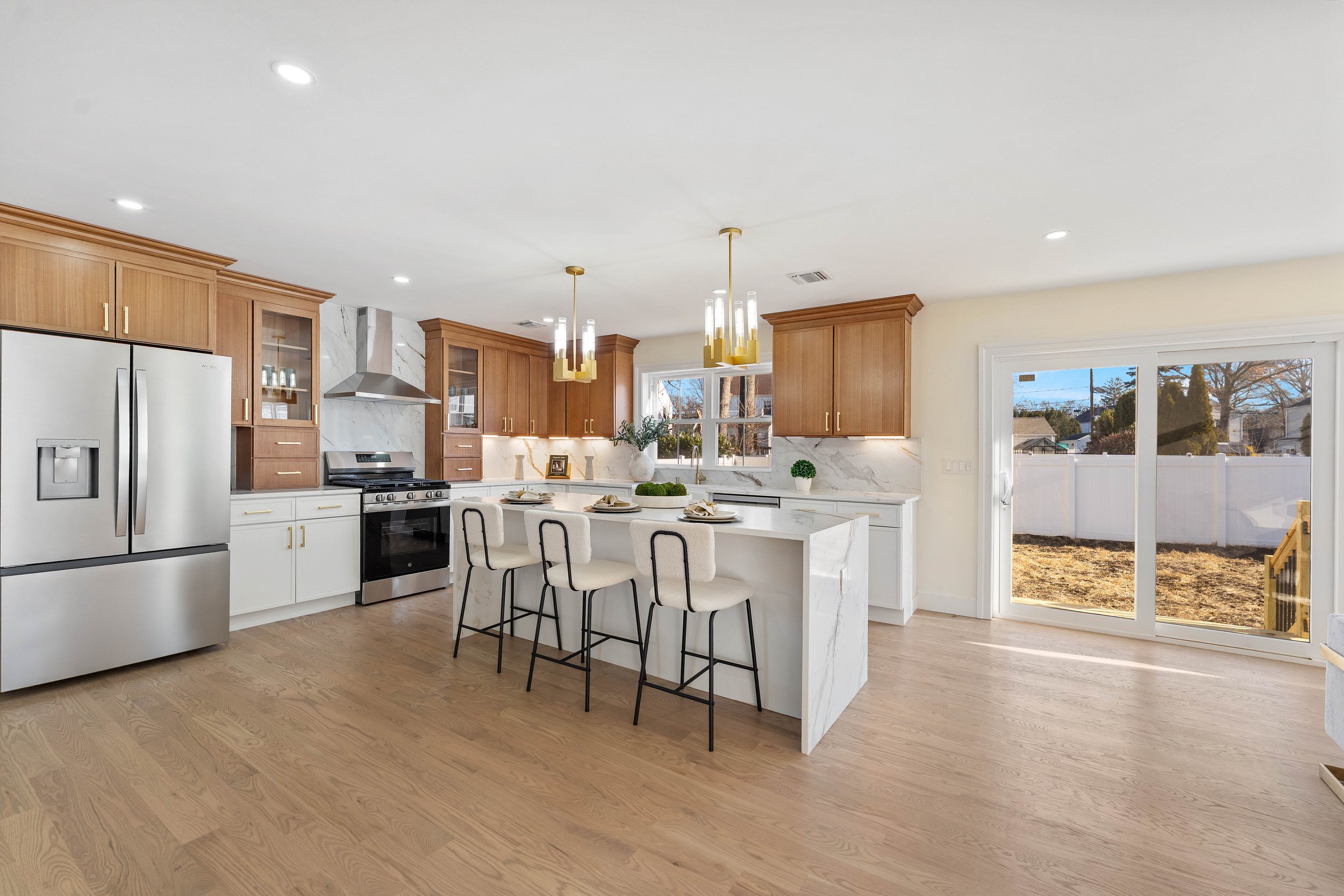 Modern kitchen with wooden cabinets, stainless steel appliances, white marble island, and a sliding glass door leading outside