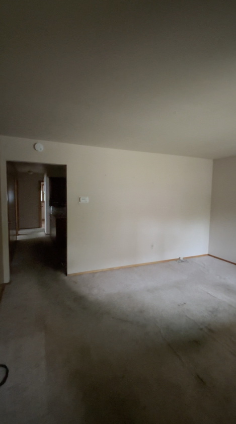 Empty living room with beige carpet, white walls, and an open doorway leading to a hallway.