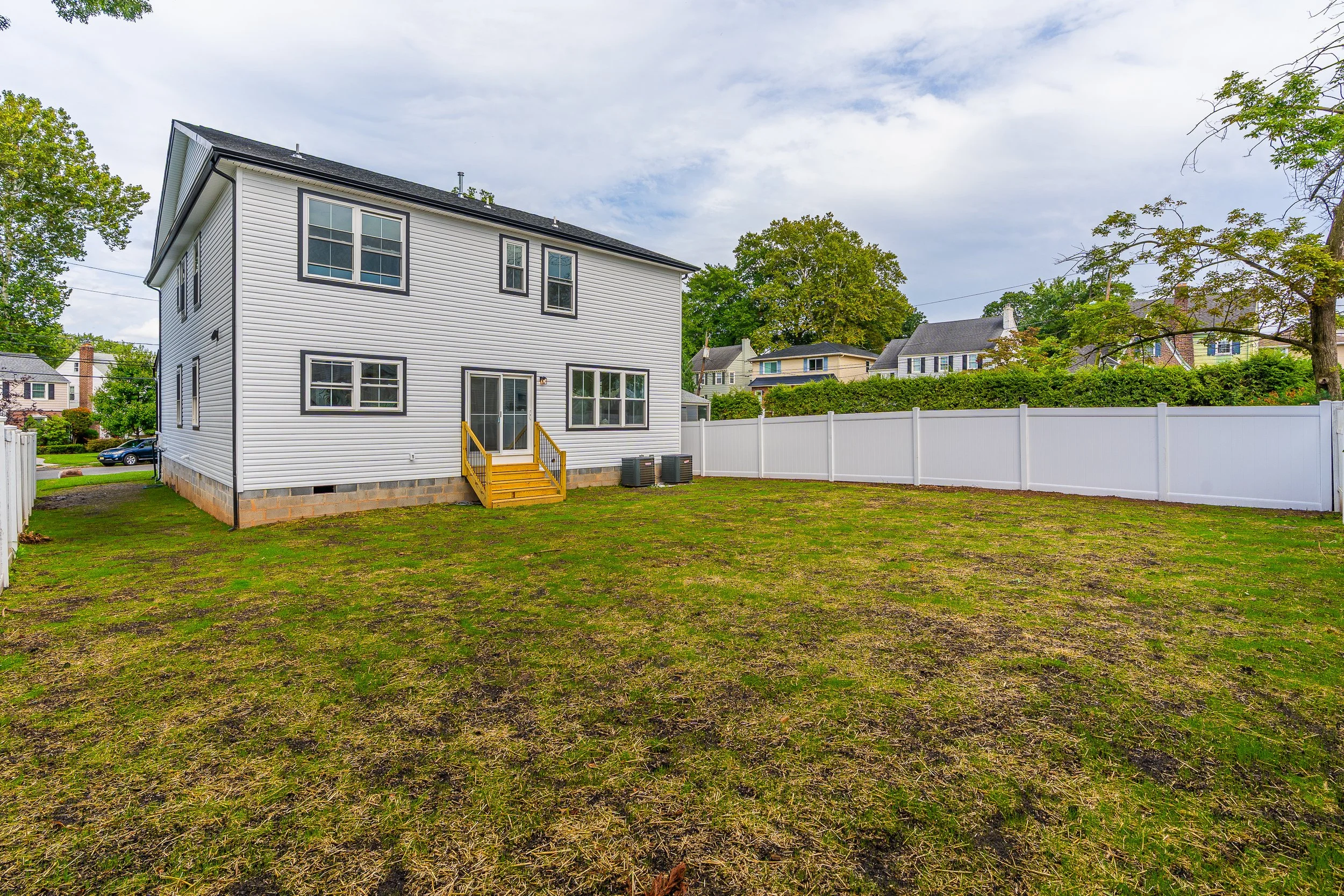 Backyard with lawn, white fence, and a two-story house with white siding and black window frames.