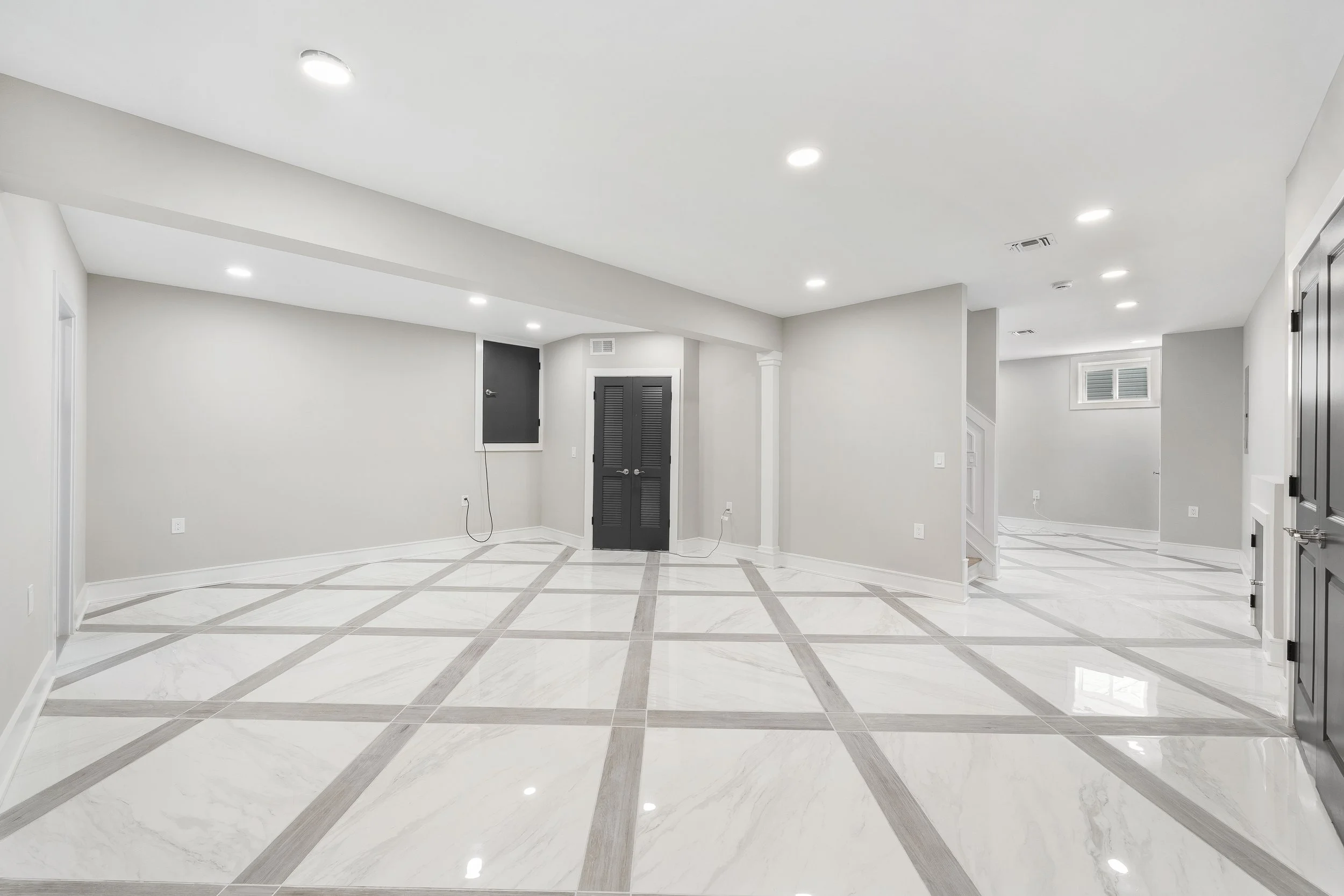 Empty modern basement with white marble tile flooring, recessed ceiling lights, and light gray walls.