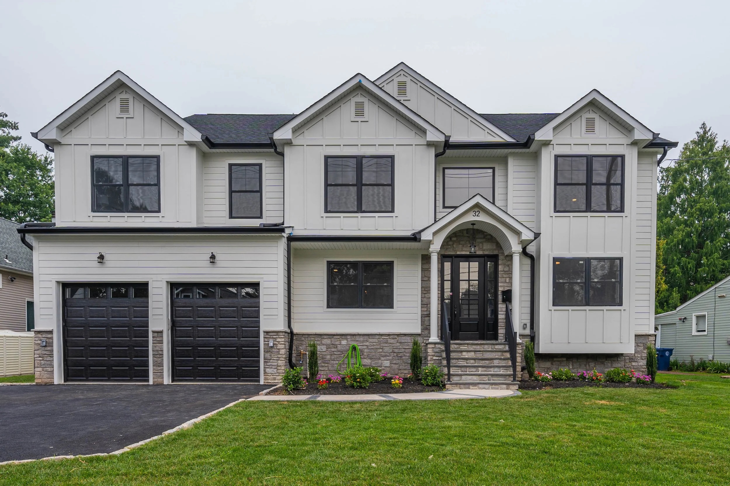 Front view of a two-story modern house with white siding, black accents, a black garage door, and a small front porch with stairs.