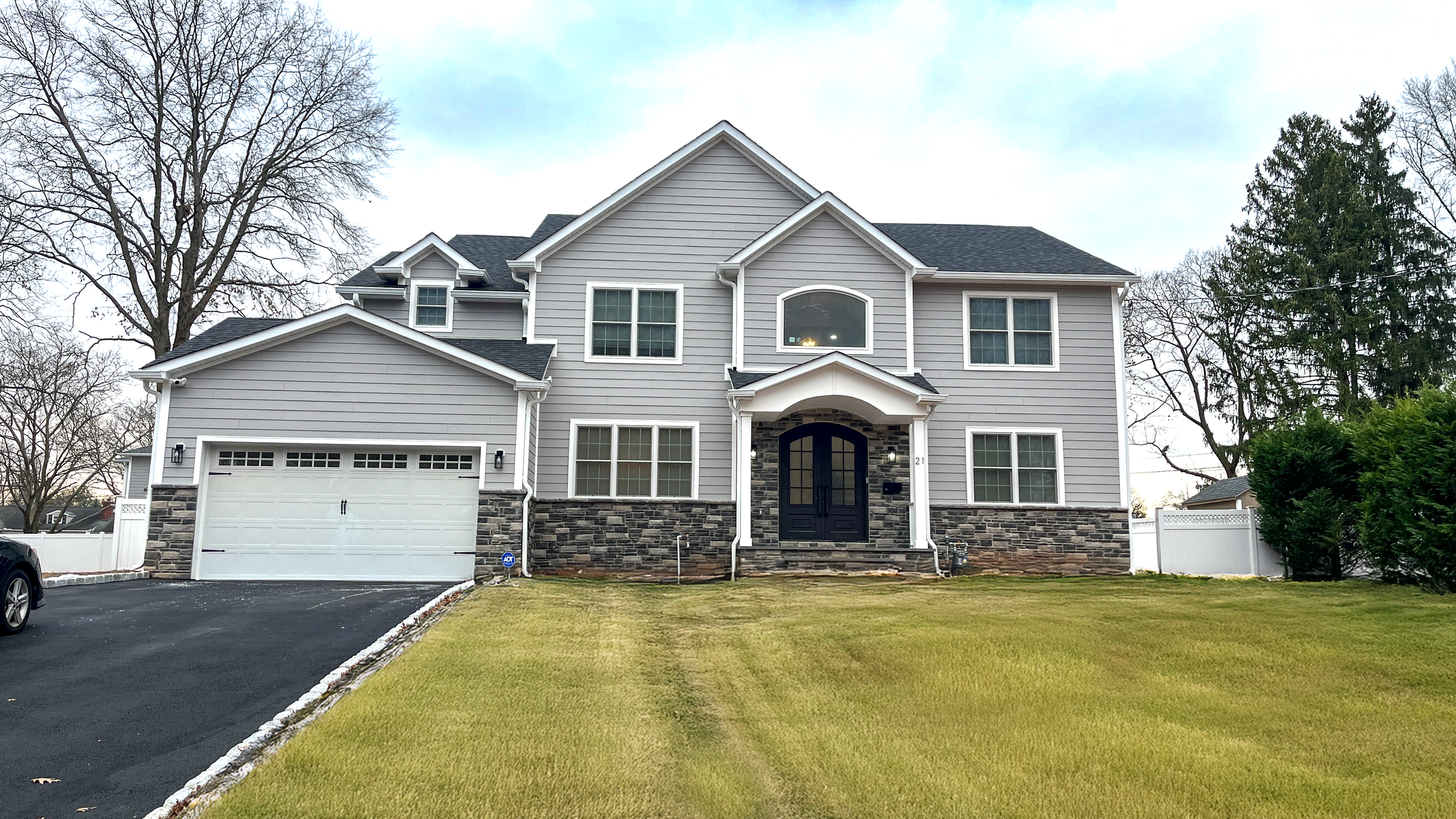 Front view of a large two-story house with gray siding, a black front door, stone accents, and a manicured lawn.