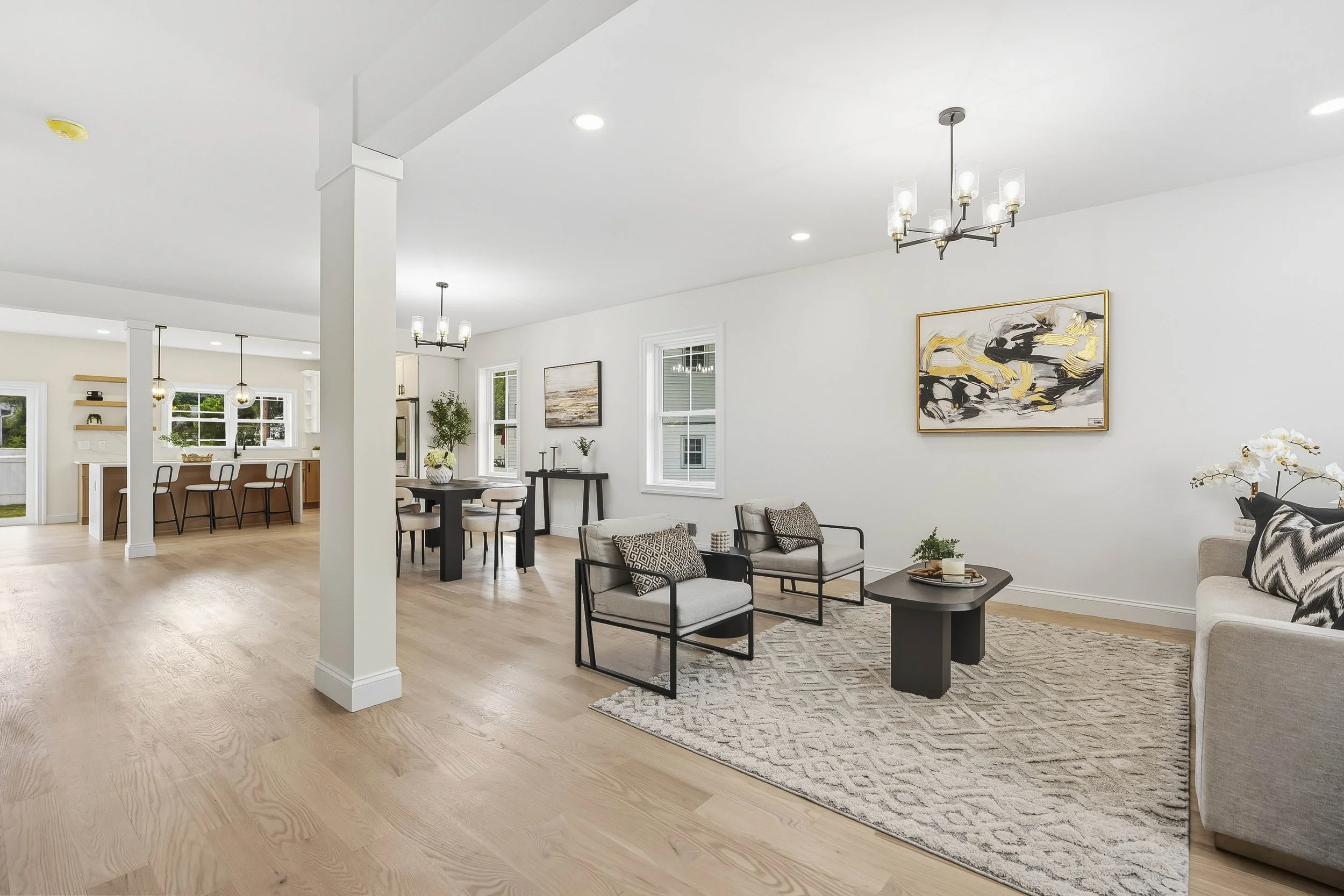 Open-concept living and dining area with light wood flooring, white walls, modern furniture, and artwork.