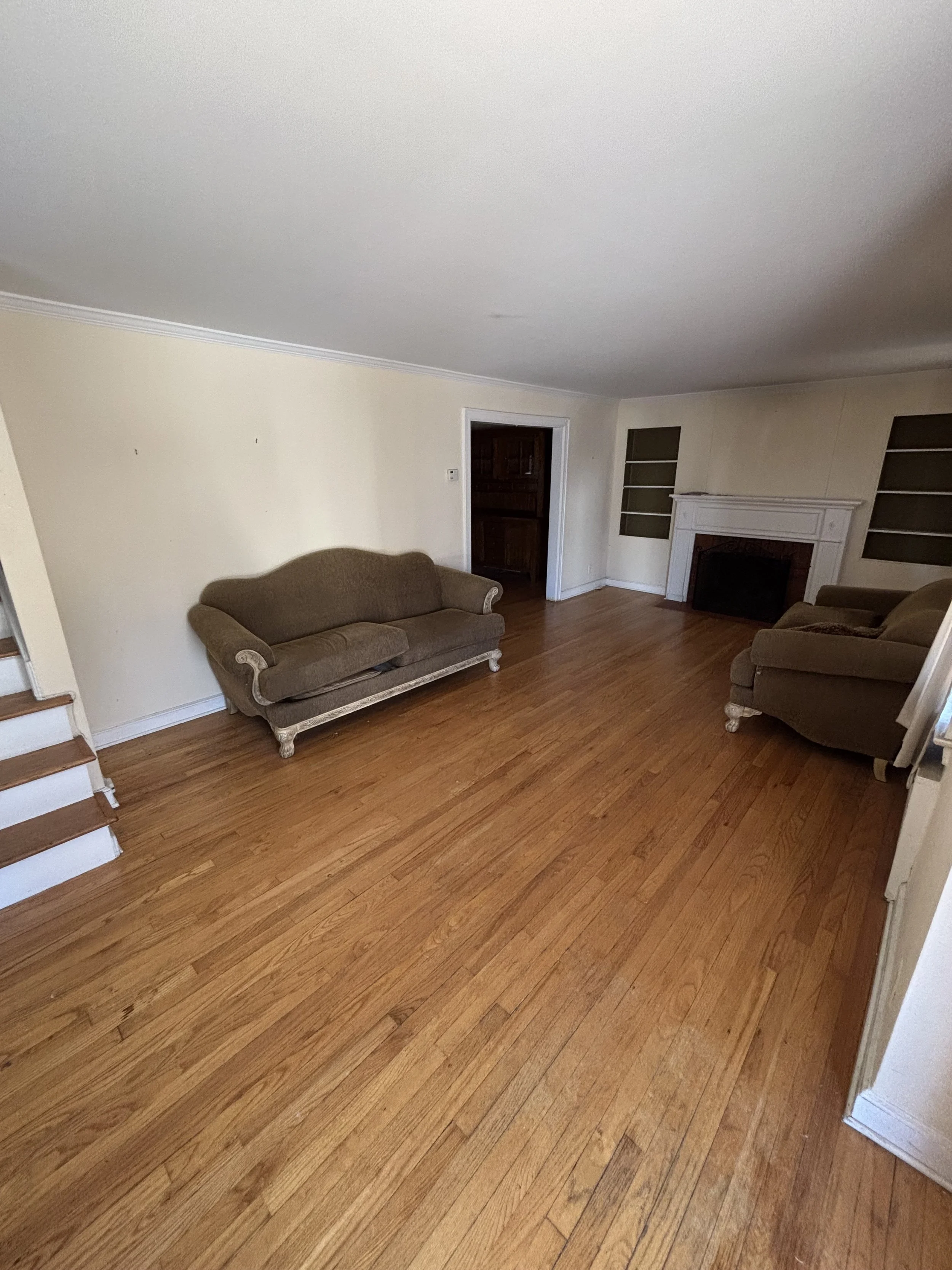Living room with hardwood floors, two brown sofas, a white fireplace with a dark interior, and built-in shelves on either side.