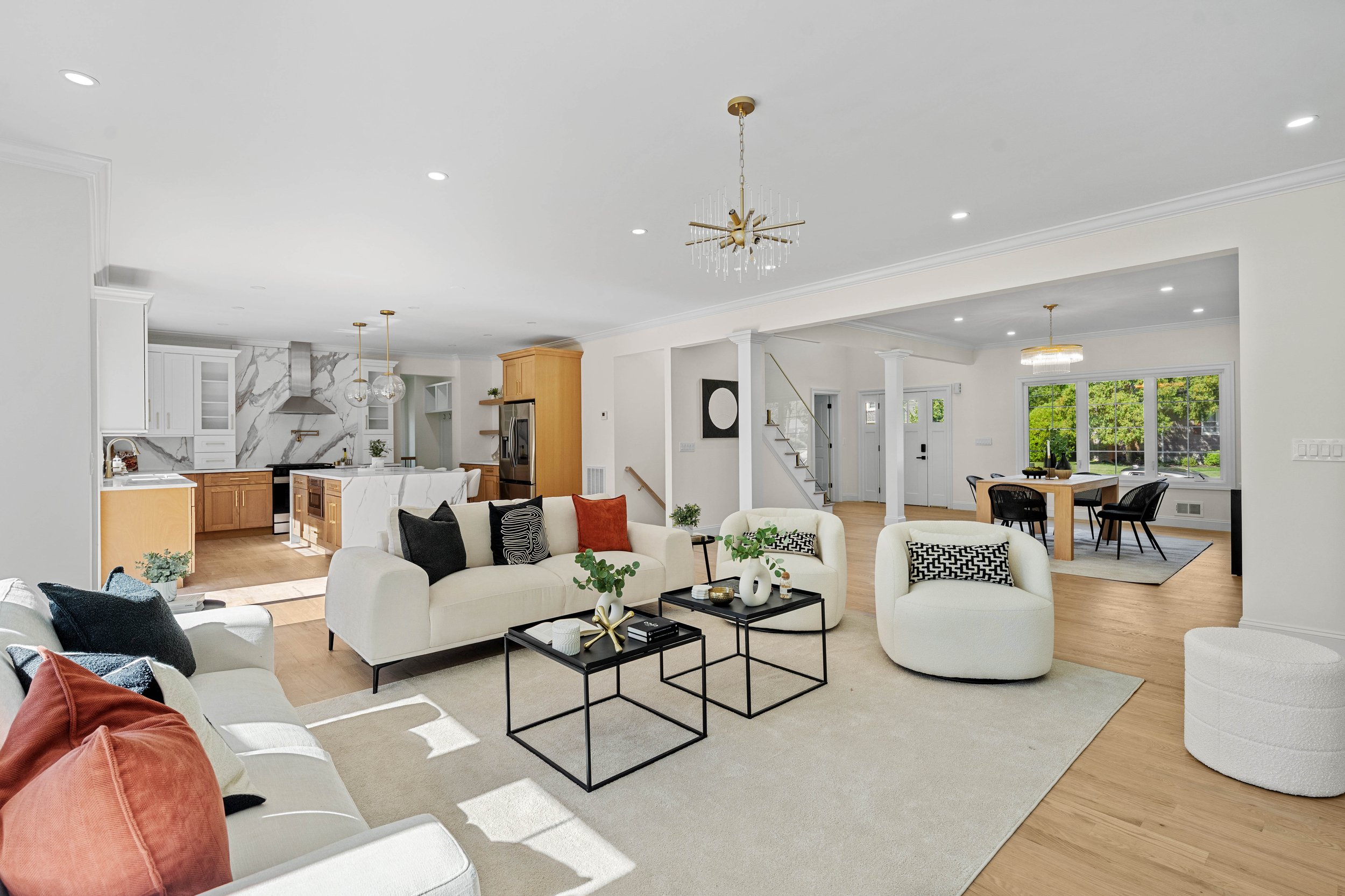 Open-concept living room and kitchen with white walls, ceiling, and furniture, wooden accents, and large windows bringing in natural light.