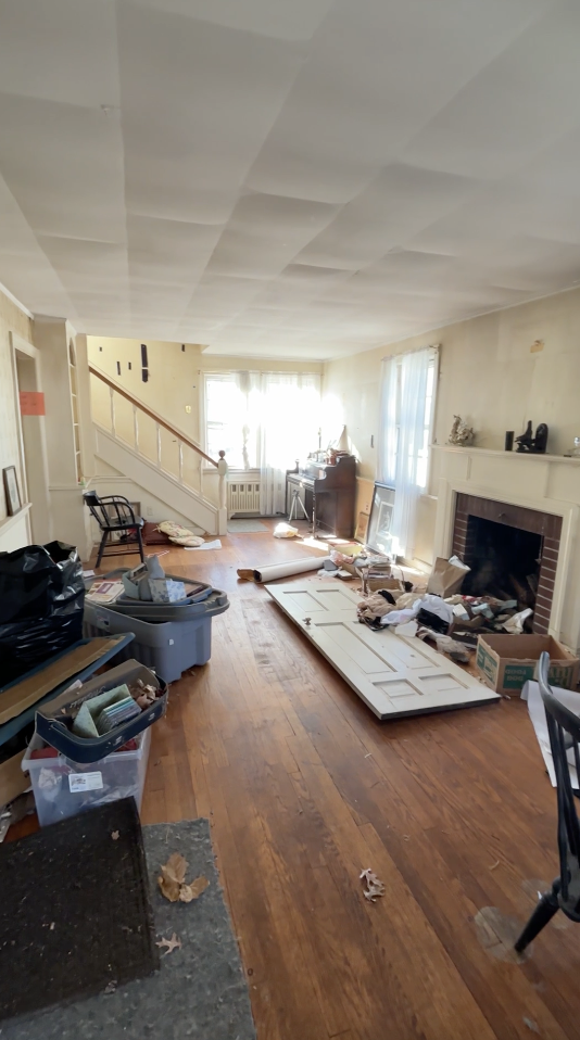 Living room with clutter, various boxes, household items, a detached door on the floor, and an unlit fireplace.