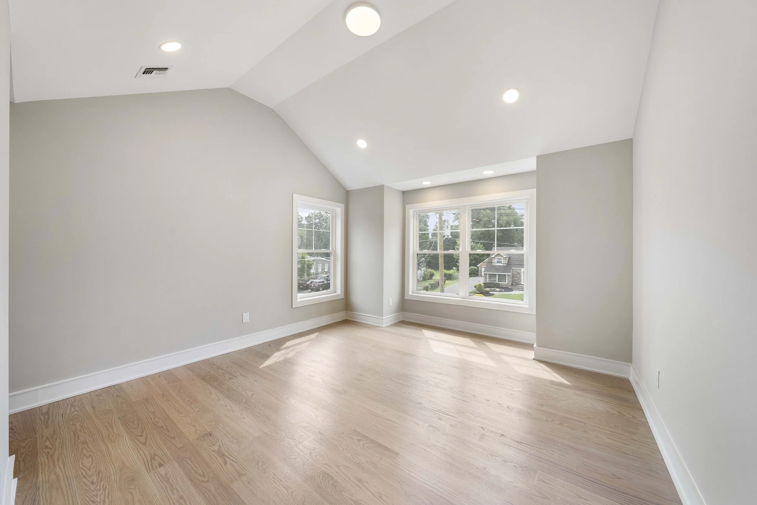 Empty room with light-colored walls, hardwood flooring, and large windows letting in natural light.