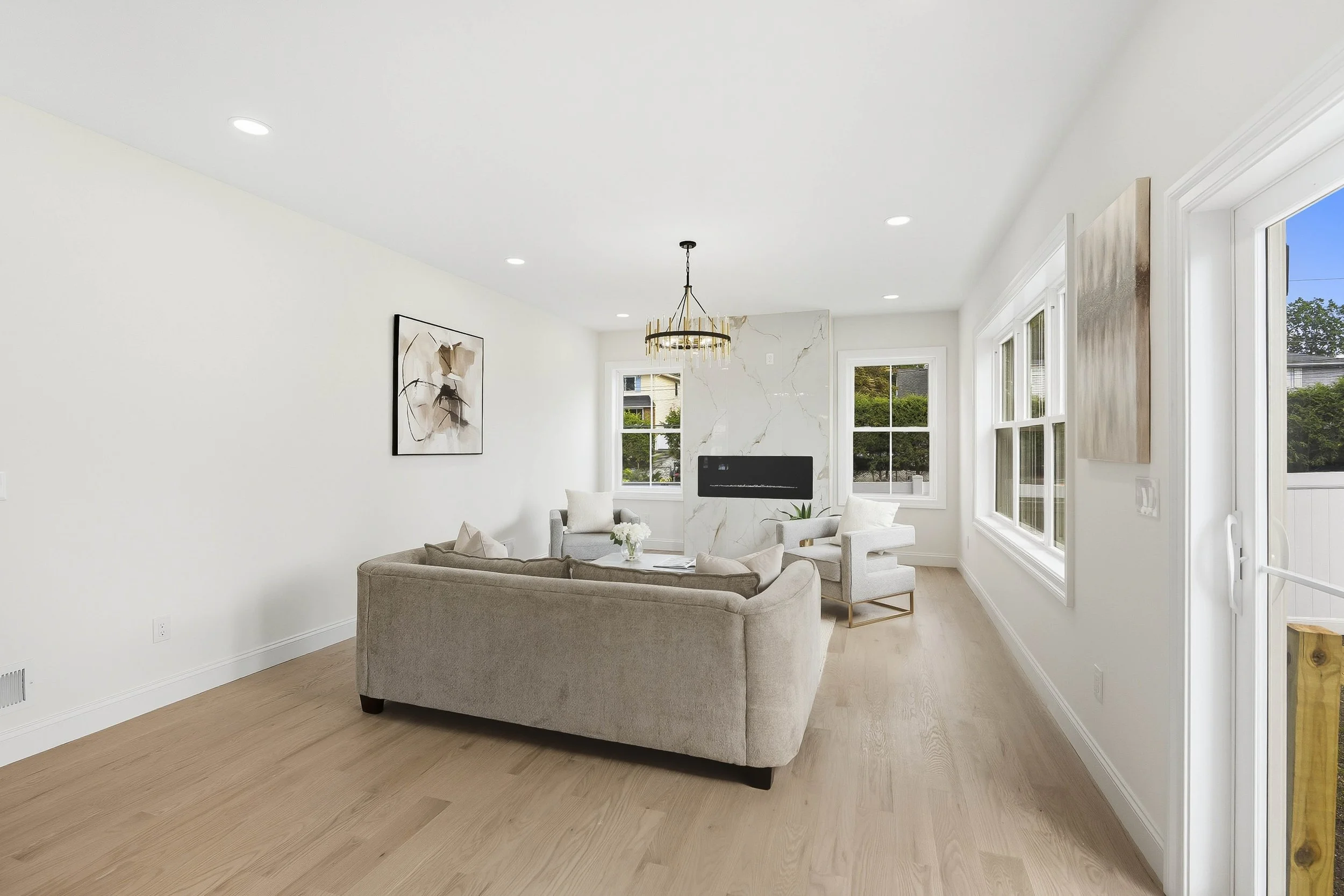 Bright living room with beige sofa, armchairs, modern fireplace, large windows, light wood flooring, and minimalist decor.