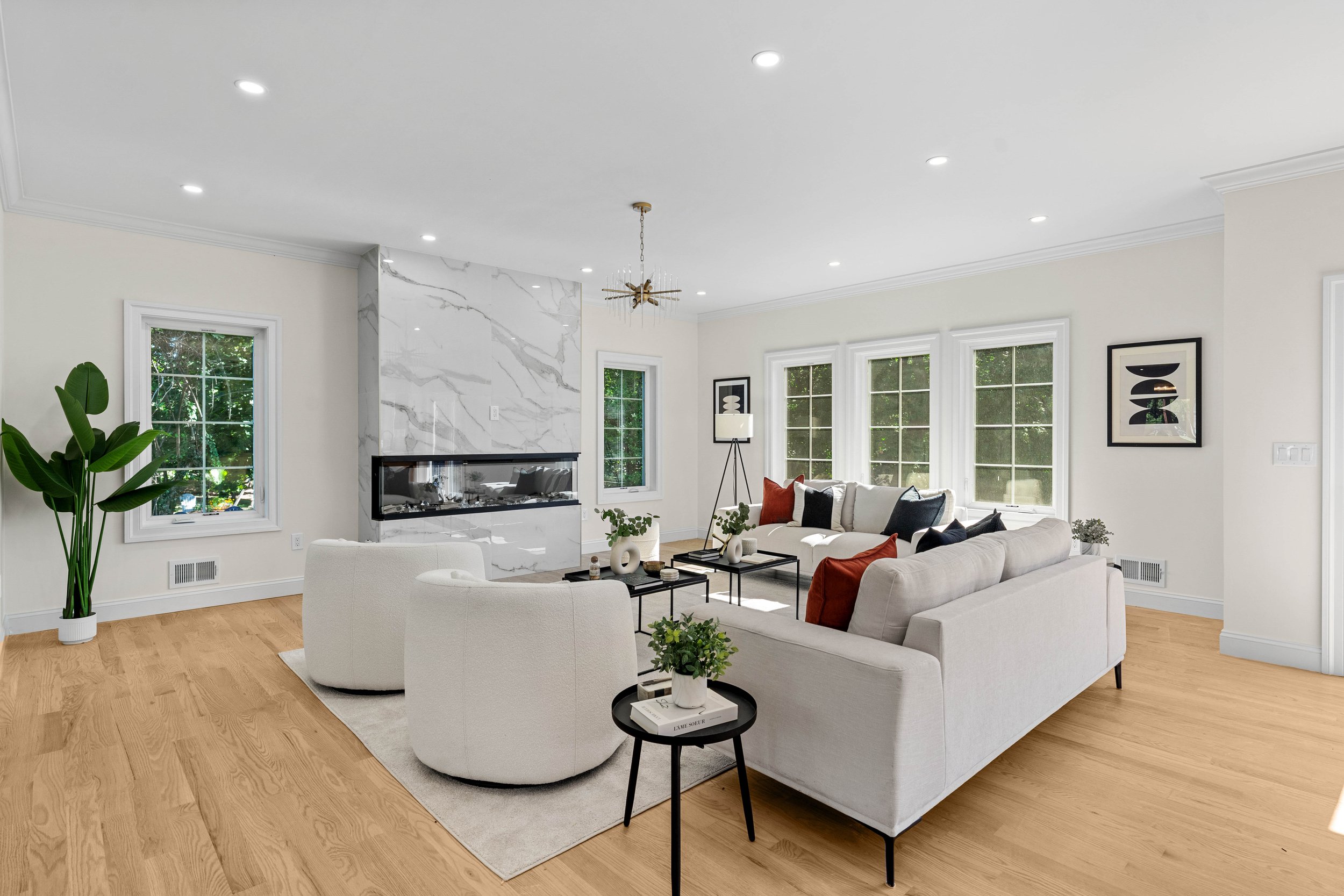 Modern living room with white sofas, black coffee tables, a fireplace with marble surround, large windows, and wooden flooring.